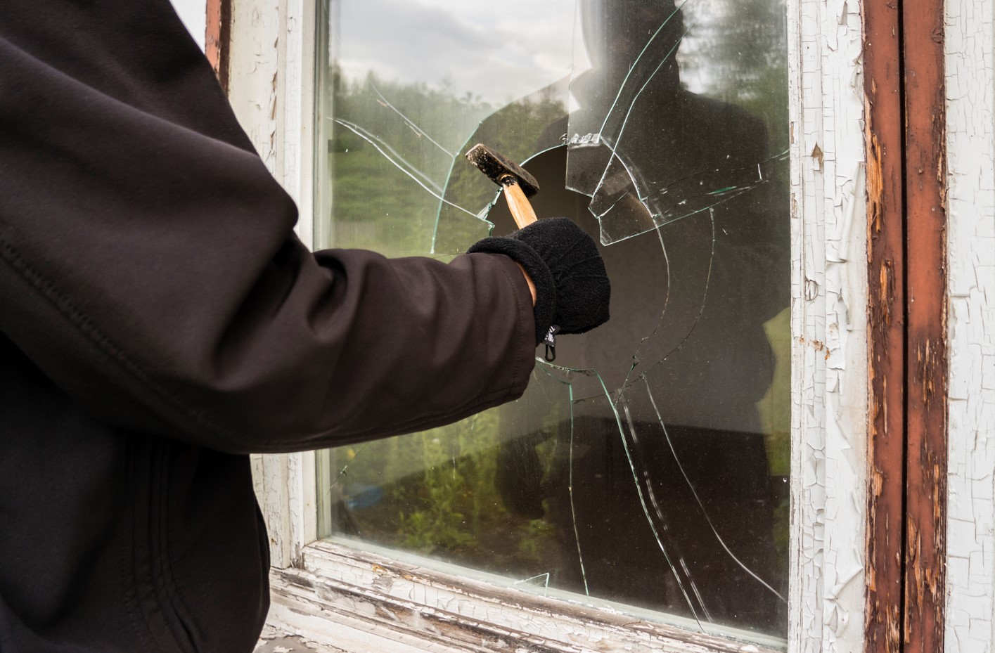 person with hammer breaking window wearing black