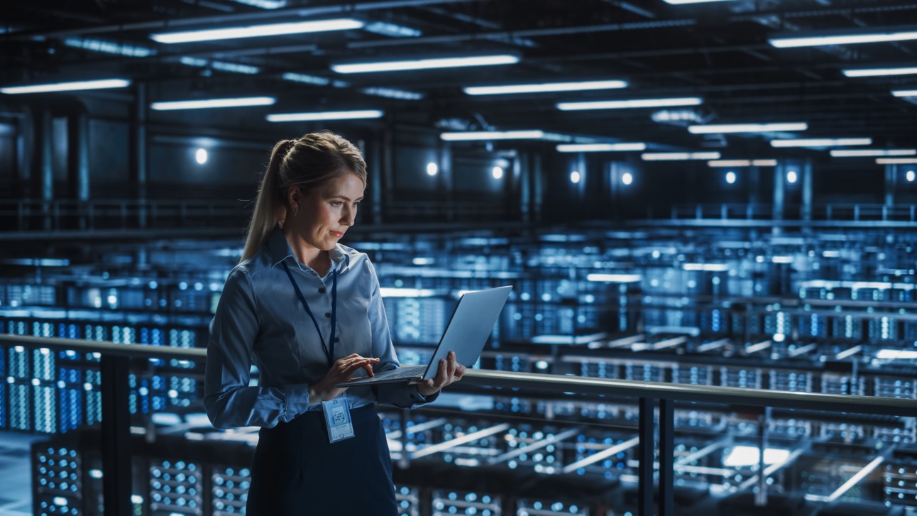 woman on laptop in front and above huge data center