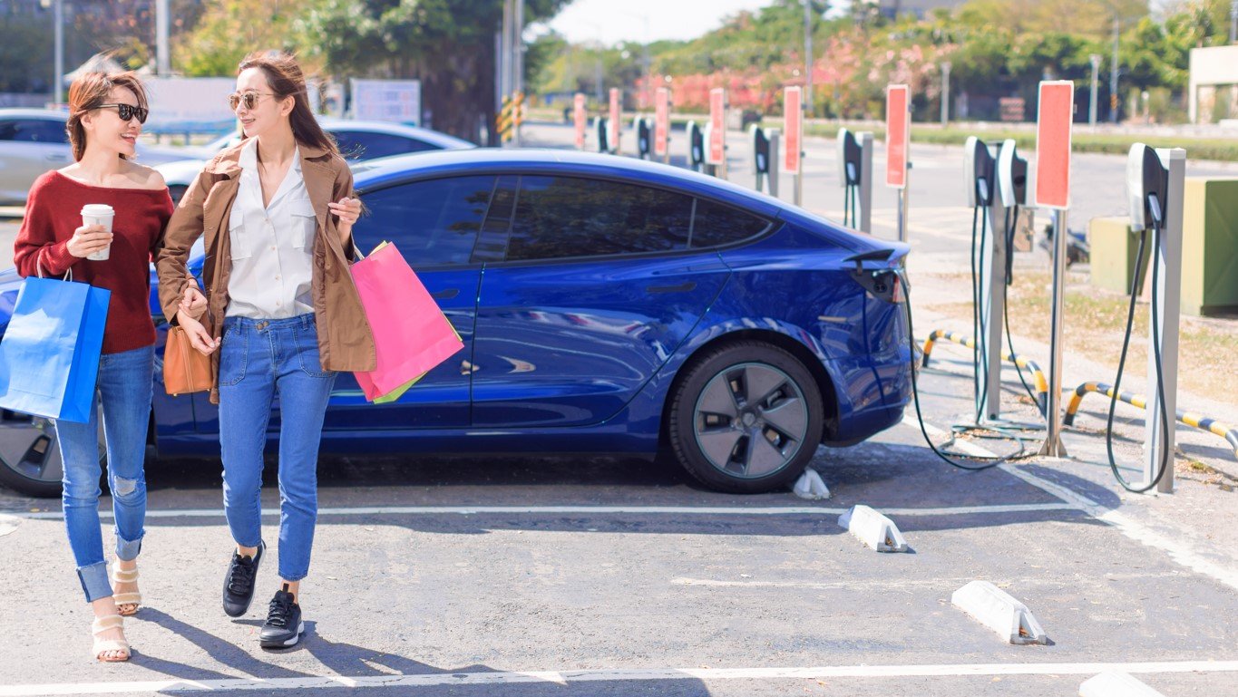two women in front of blue tesla at charging station
