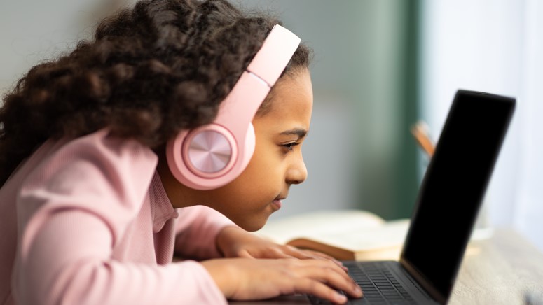 girl wearing headphones and pink outfit looks at laptop screen