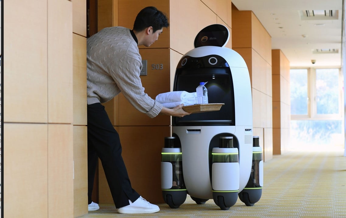 man takes item from delivery robot in hotel hallway