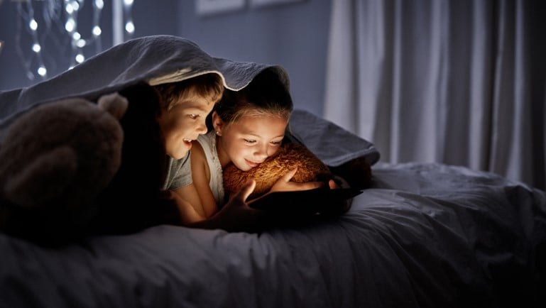 two boys under covers on tablet