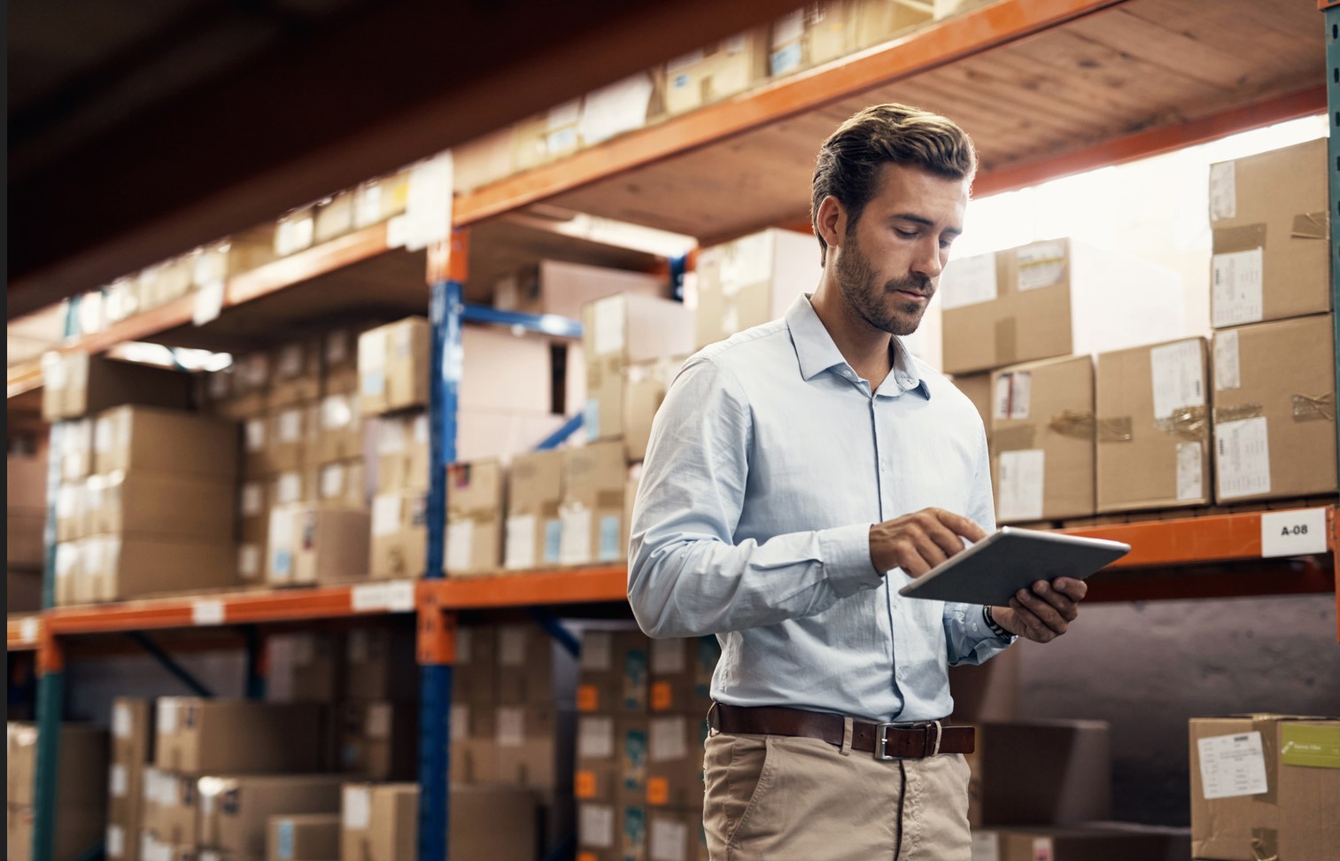 man walking with tablet in front of boxes on warehouse shelves