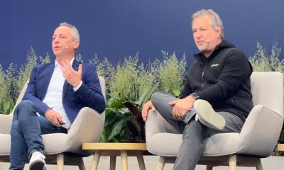 Two men sit on stage in modern armchairs during a panel discussion.