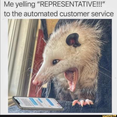 An opossum with its mouth wide open appears to be yelling at a smartphone screen, which is lying flat in front of it and displaying a chat interface. The text above the image reads: “Me yelling ‘REPRESENTATIVE!!!’ to the automated customer service.” The opossum’s expression looks frustrated or angry.