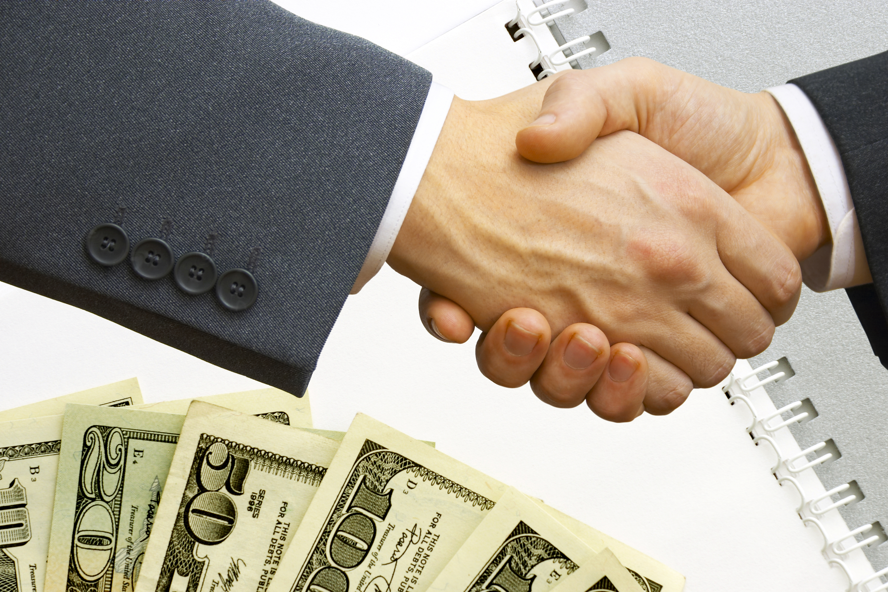 Two businessmen shaking hands over a pile of money
