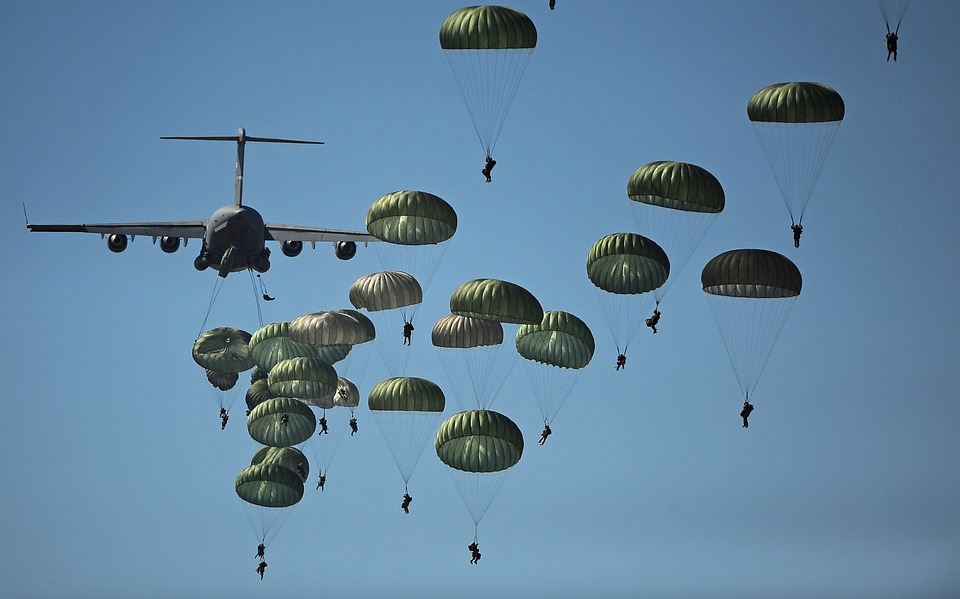 Many people jumping out of a plane with green parachutes