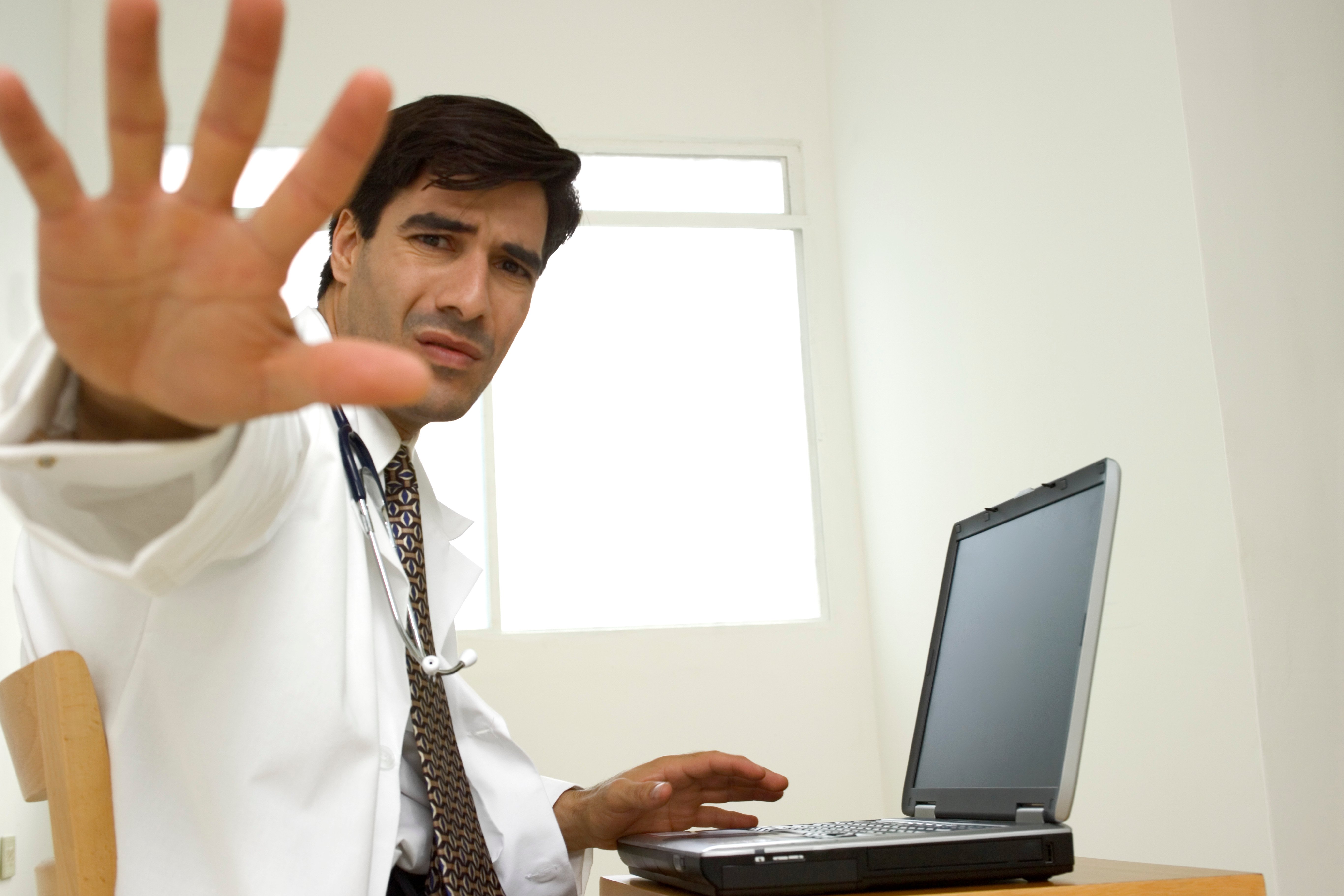 A doctor at a desk holding up his hand to say stop