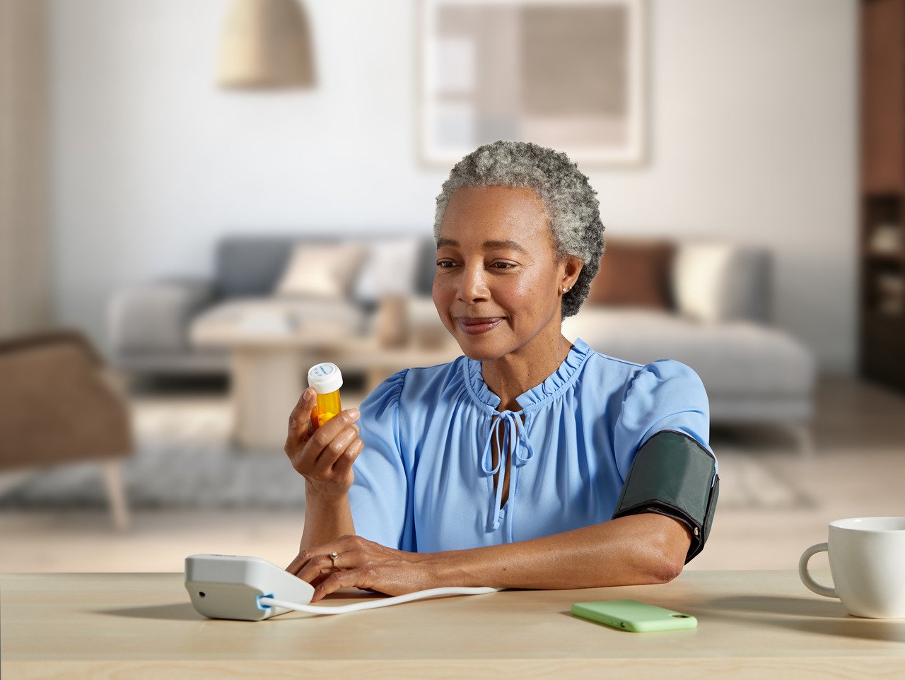 senior woman taking blood pressure at home and holding medication bottle
