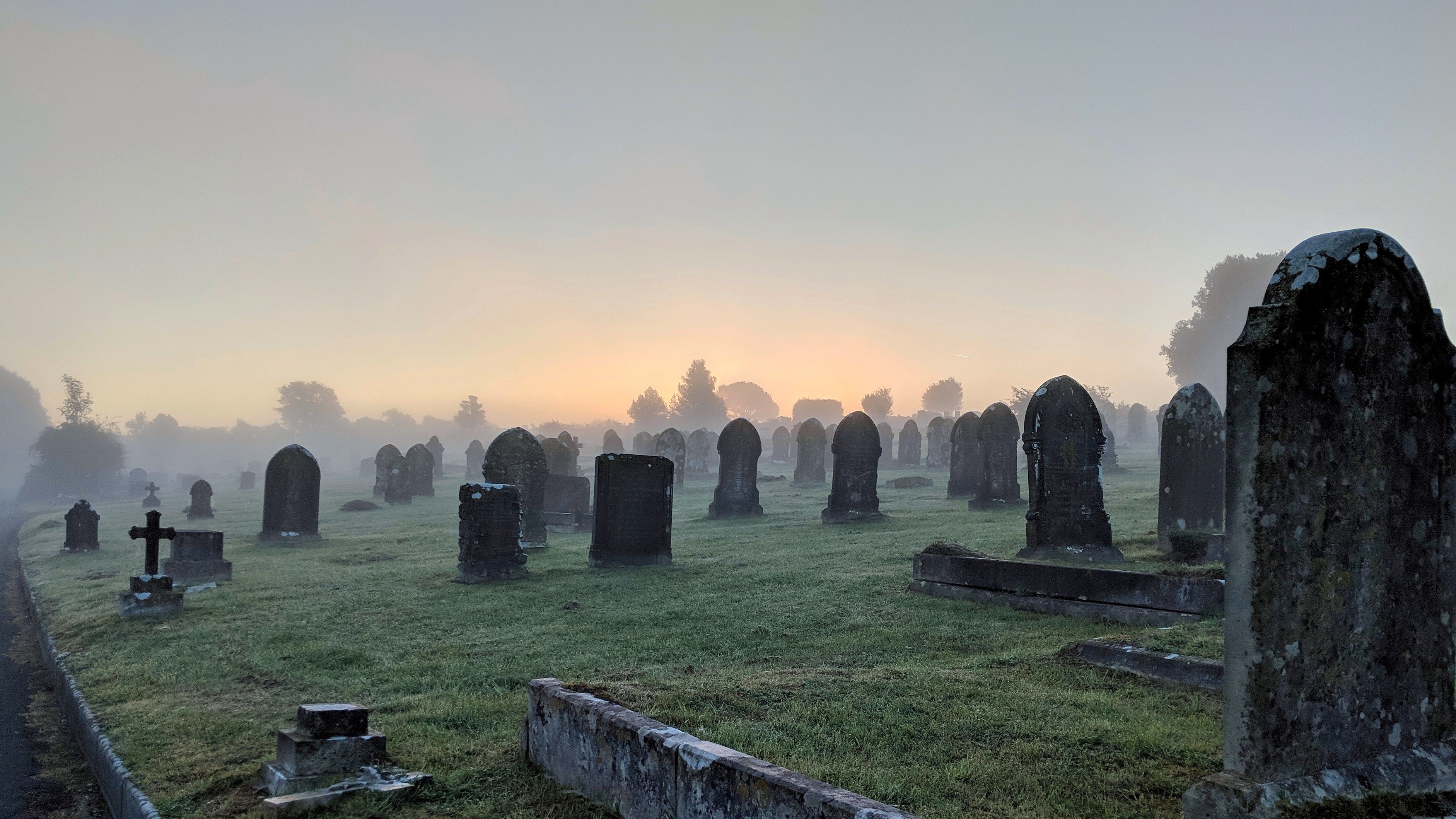 Photo of a misty graveyard at dawn with the first glimpse of sunlight on the horizon