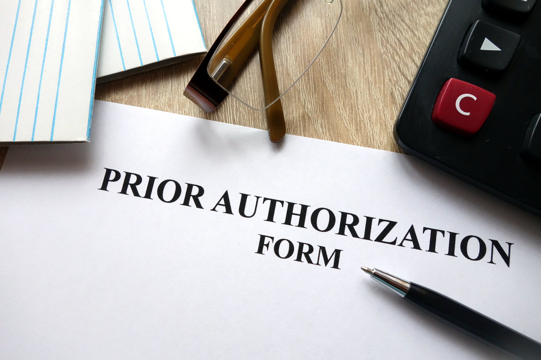 Prior authorization paperwork next to a calculator and pair of glasses