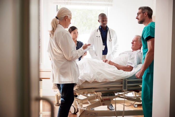 doctor and medical team on rounds meeting around bed of senior male patient