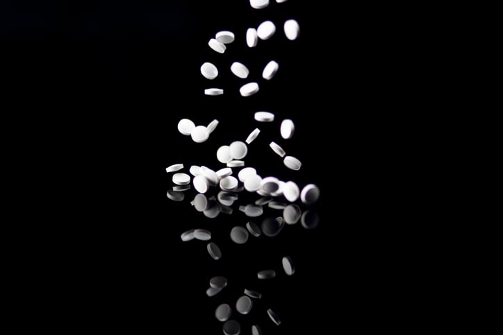White pills falling on a black background with reflection