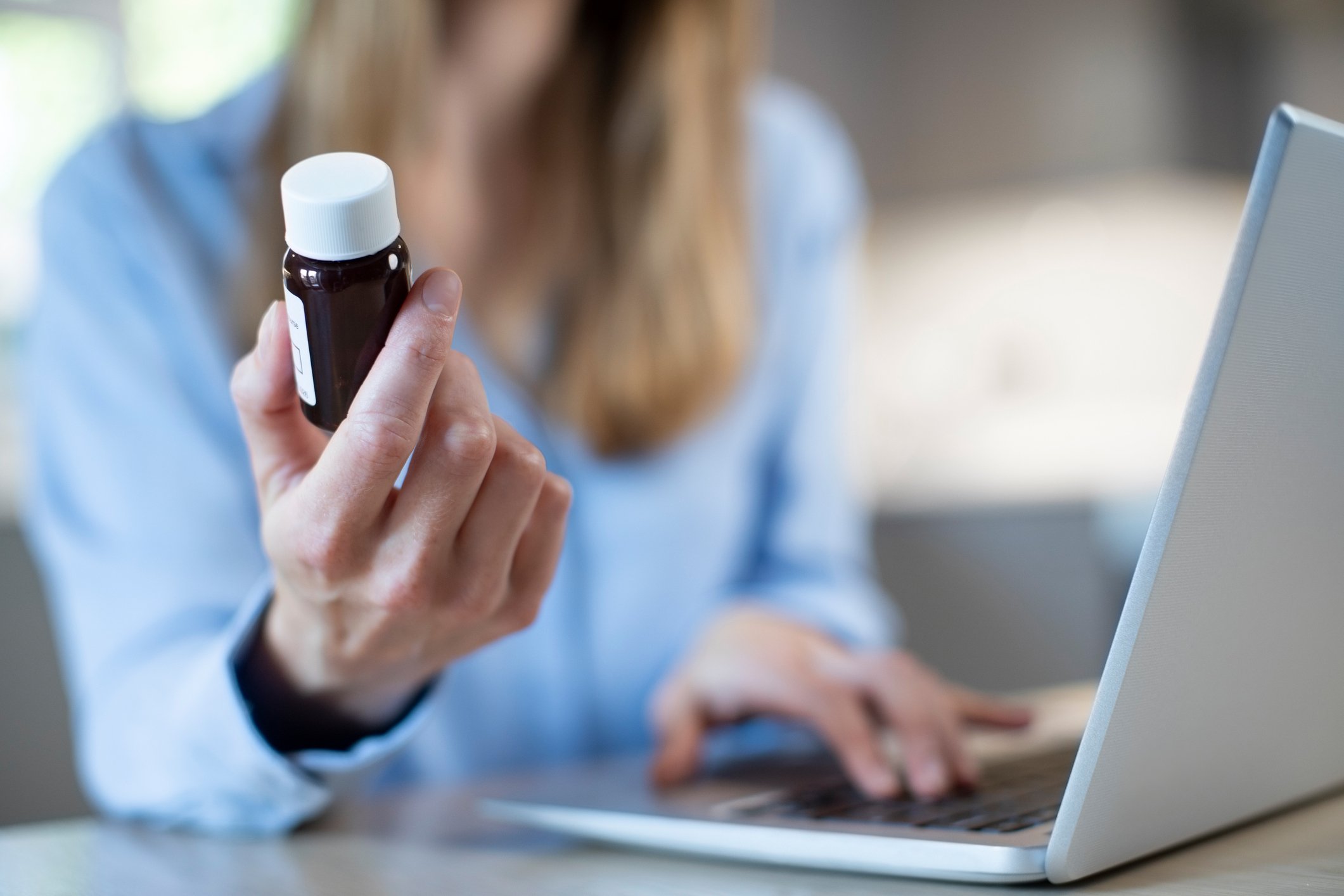 Woman holding up pill bottle with laptop