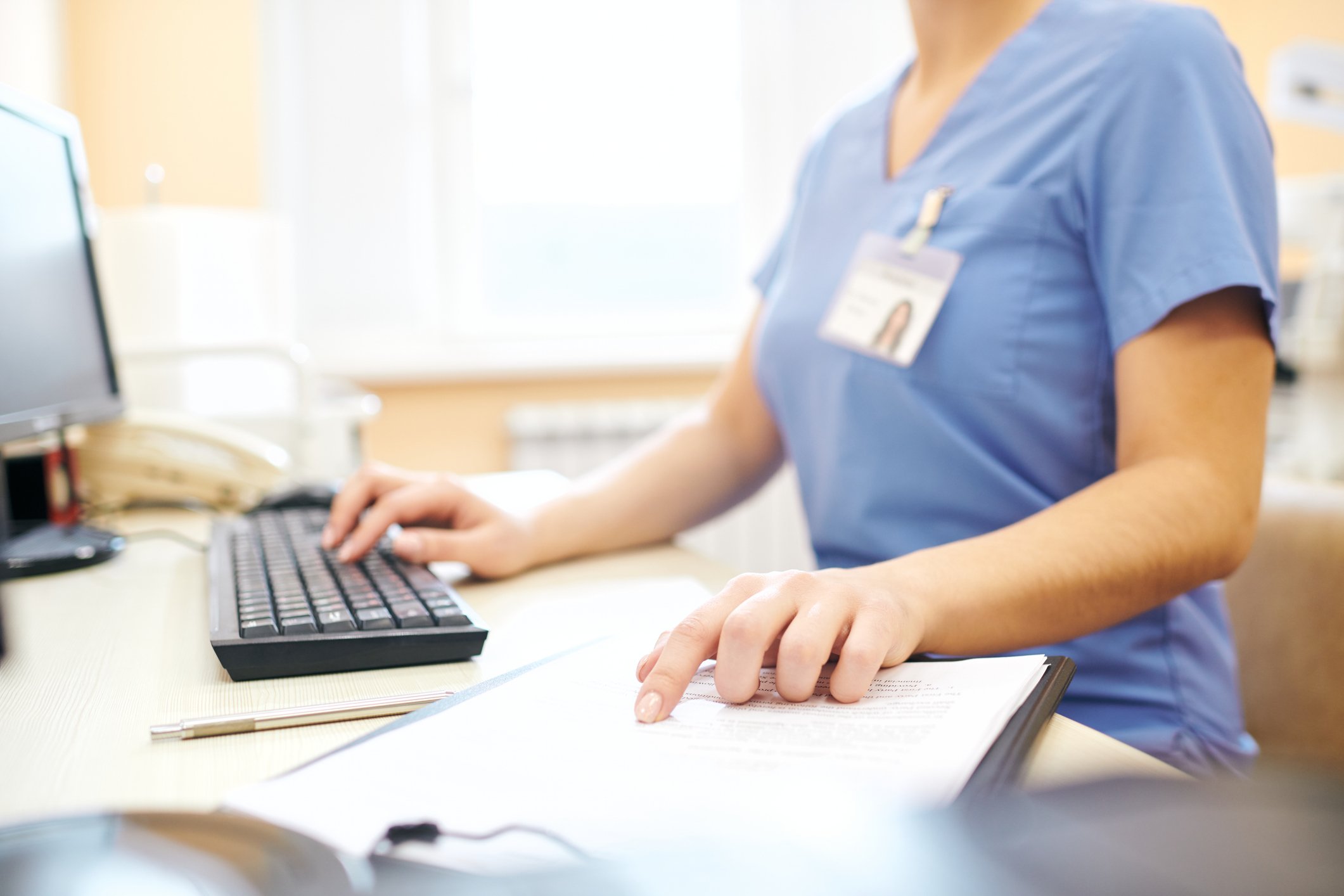 Nurse sitting at desk and using computer while analyzing medical notes