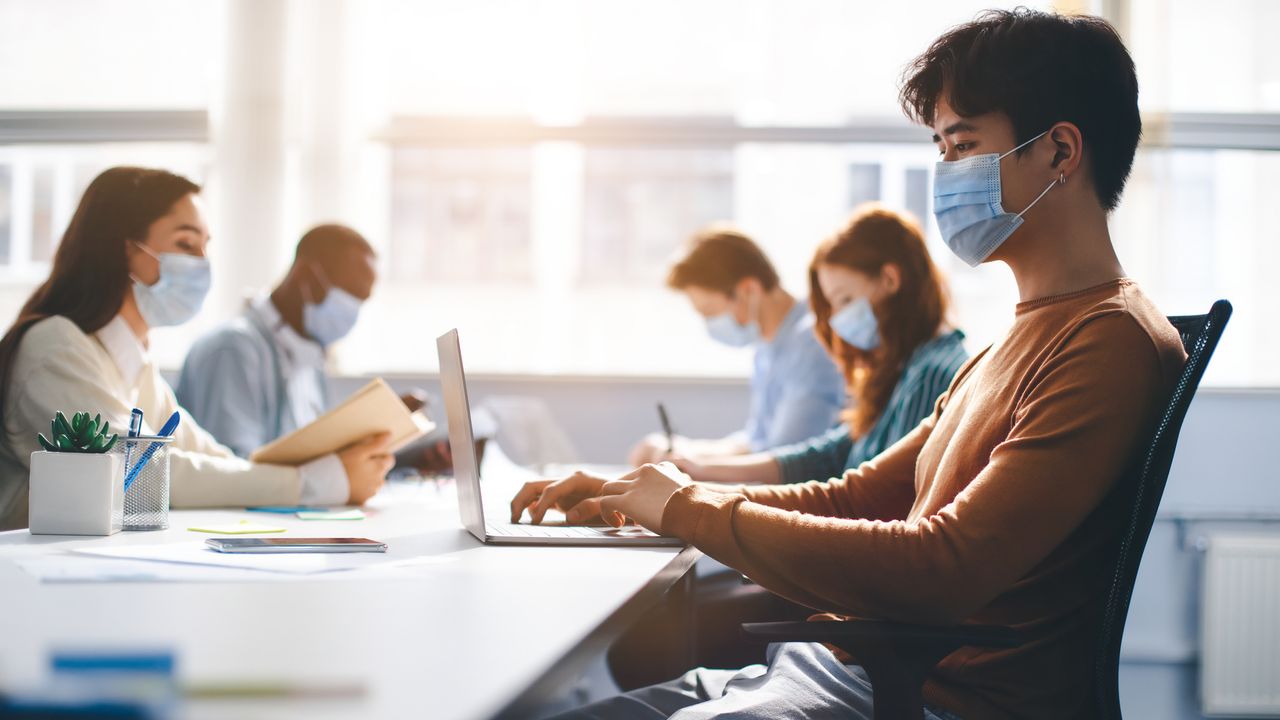 employees wearing protective medical masks and using laptop computers