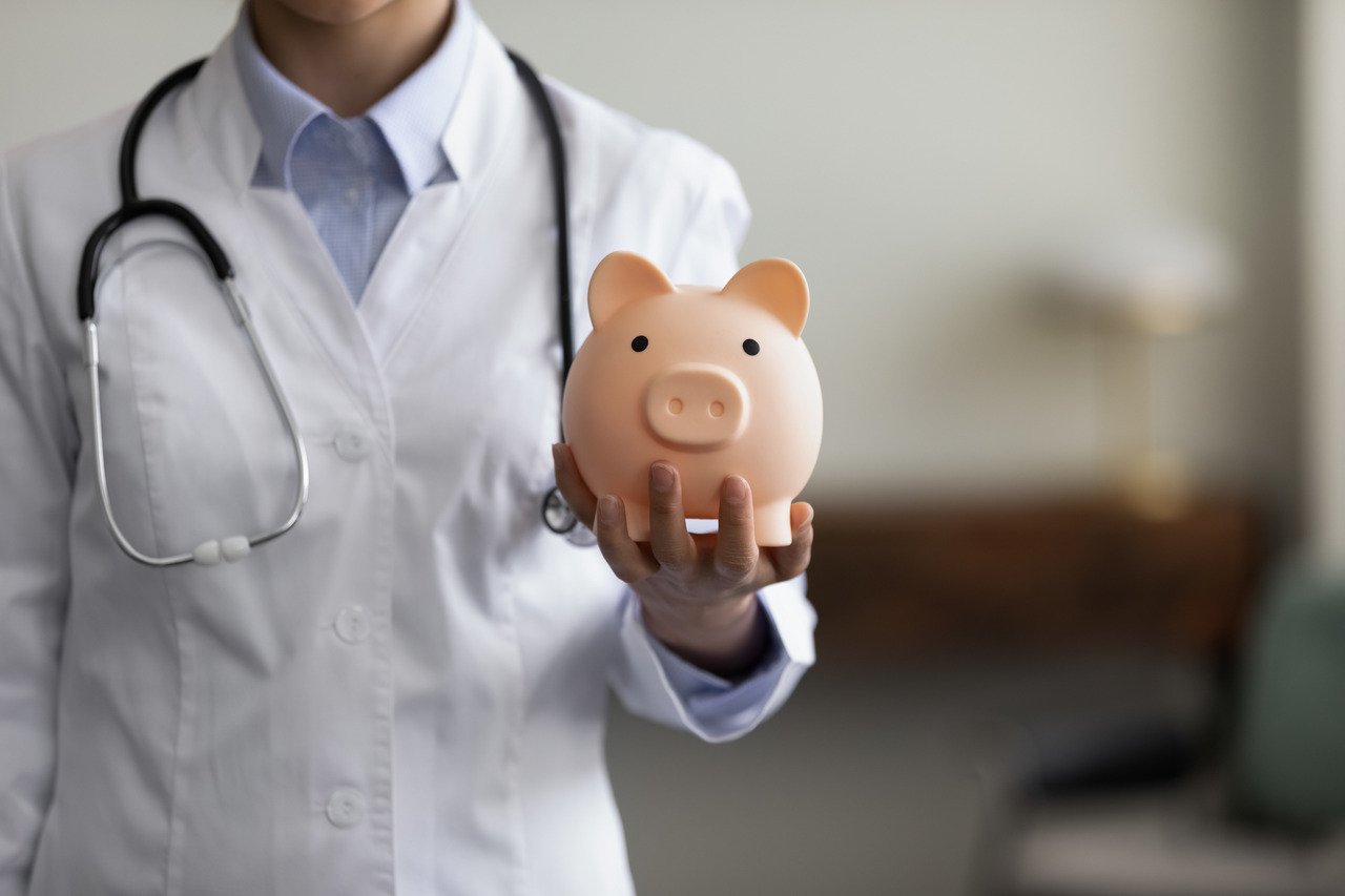 female doctor physician nurse in white uniform with stethoscope holding pink piggy bank in hand