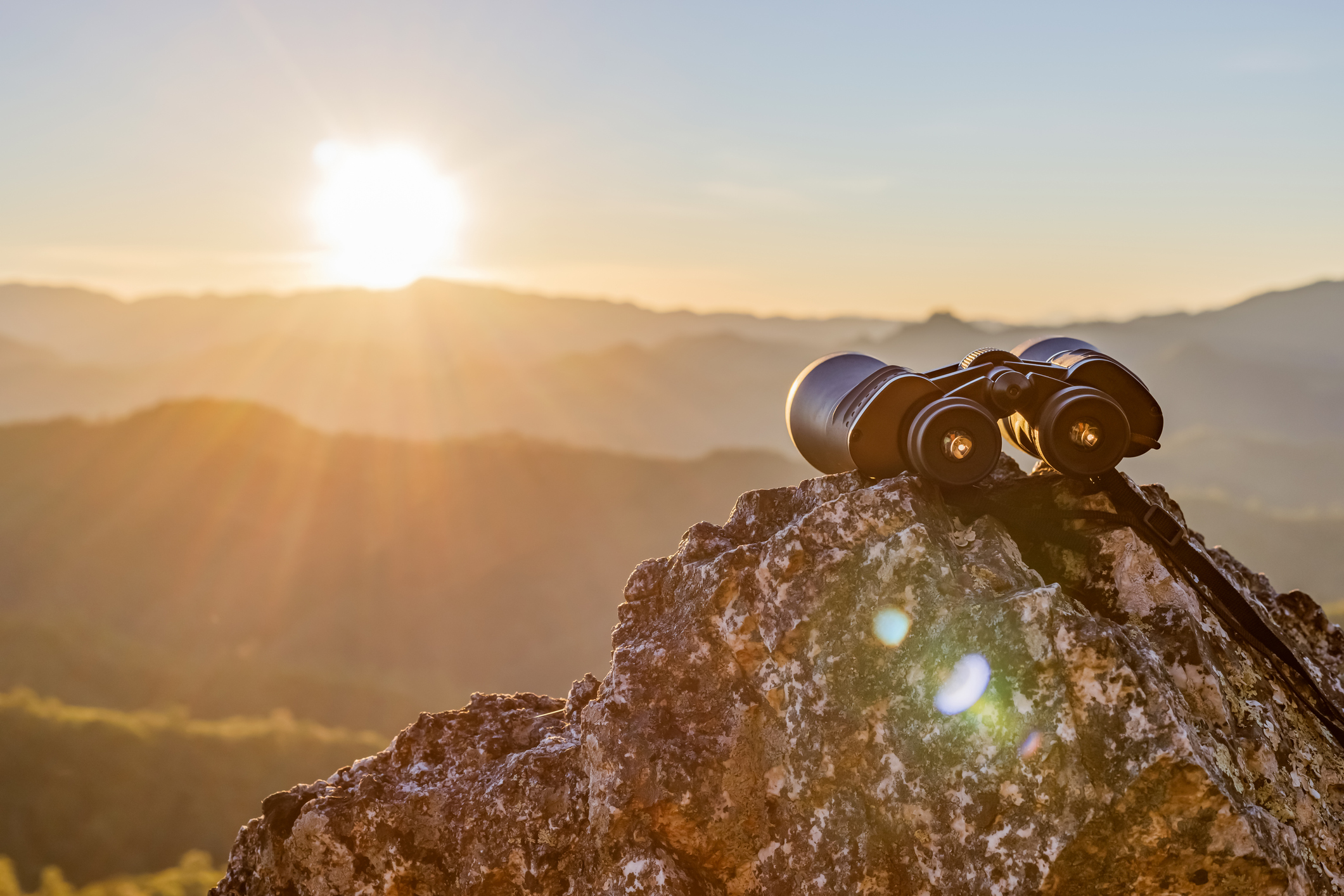 photo of a pair of binoculars perched on a rock aimed at the rising sun