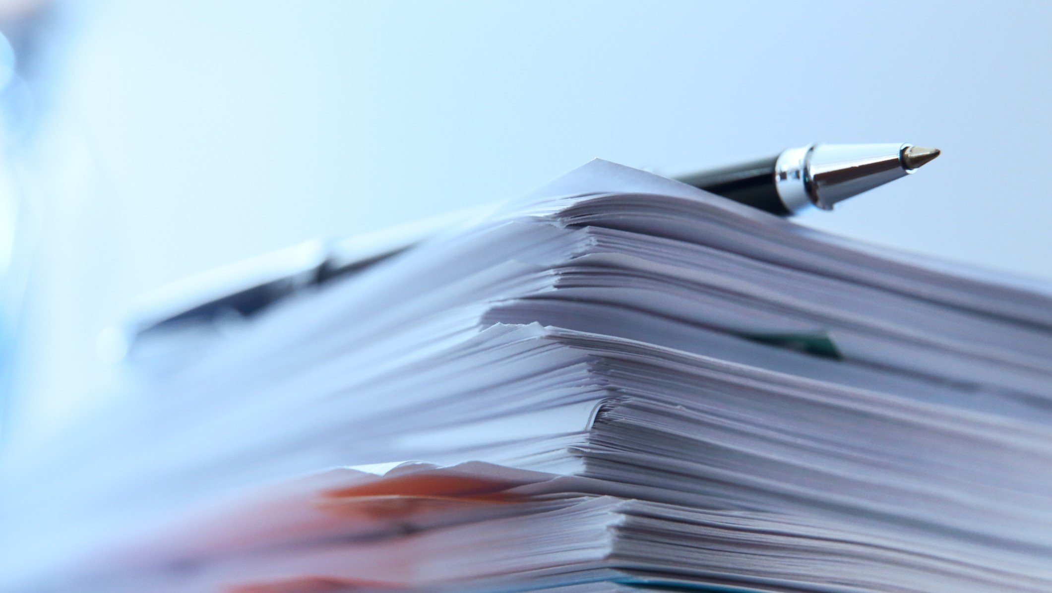 A ballpoint pen rests on top of a stack of documents ready for signing