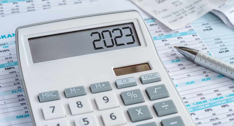 A calculator reads 2023 and sits on a stick of financial forms