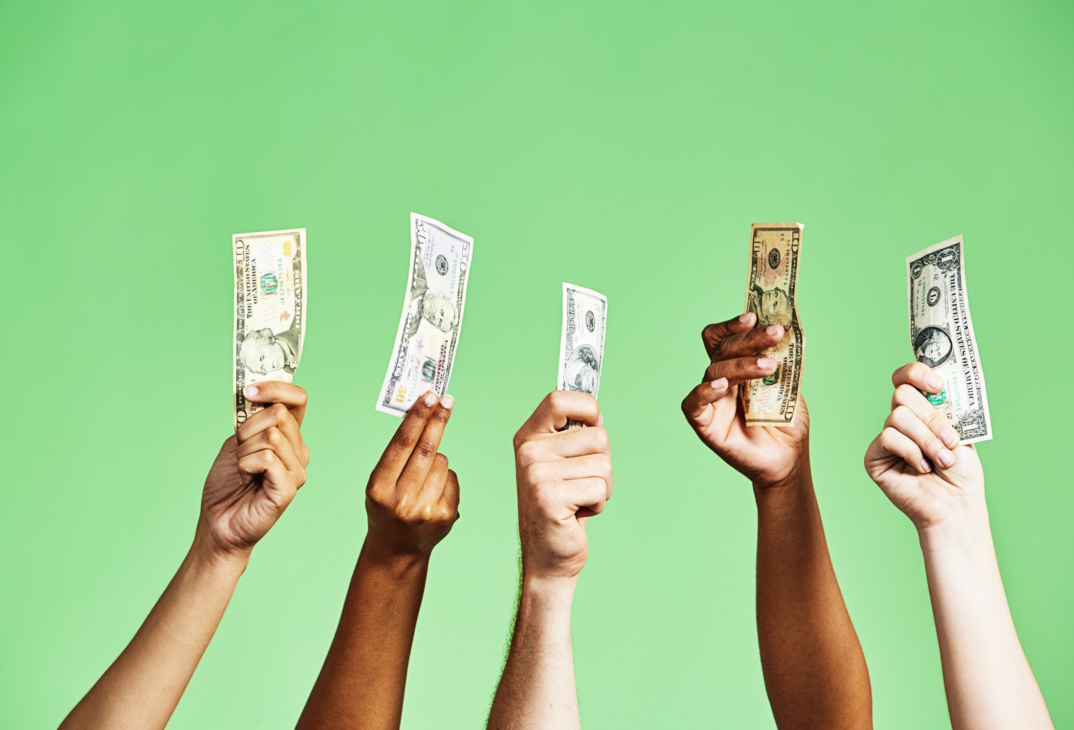 Diverse group of hands holding up US dollar banknotes of various denominations on green background - stock photo