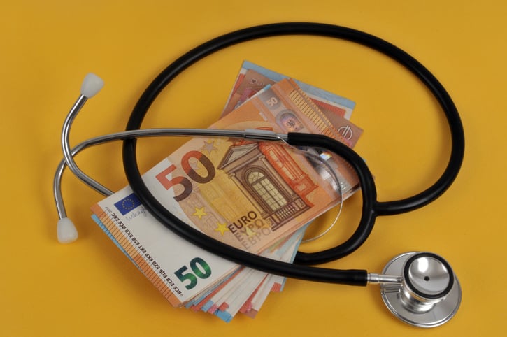 A stack of euro bills and a stethoscope on a yellow background