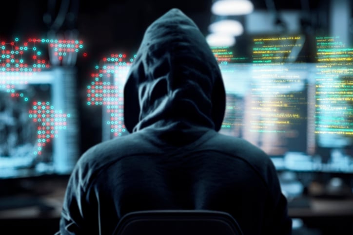 A computer hacker in a sweatshirt examines data