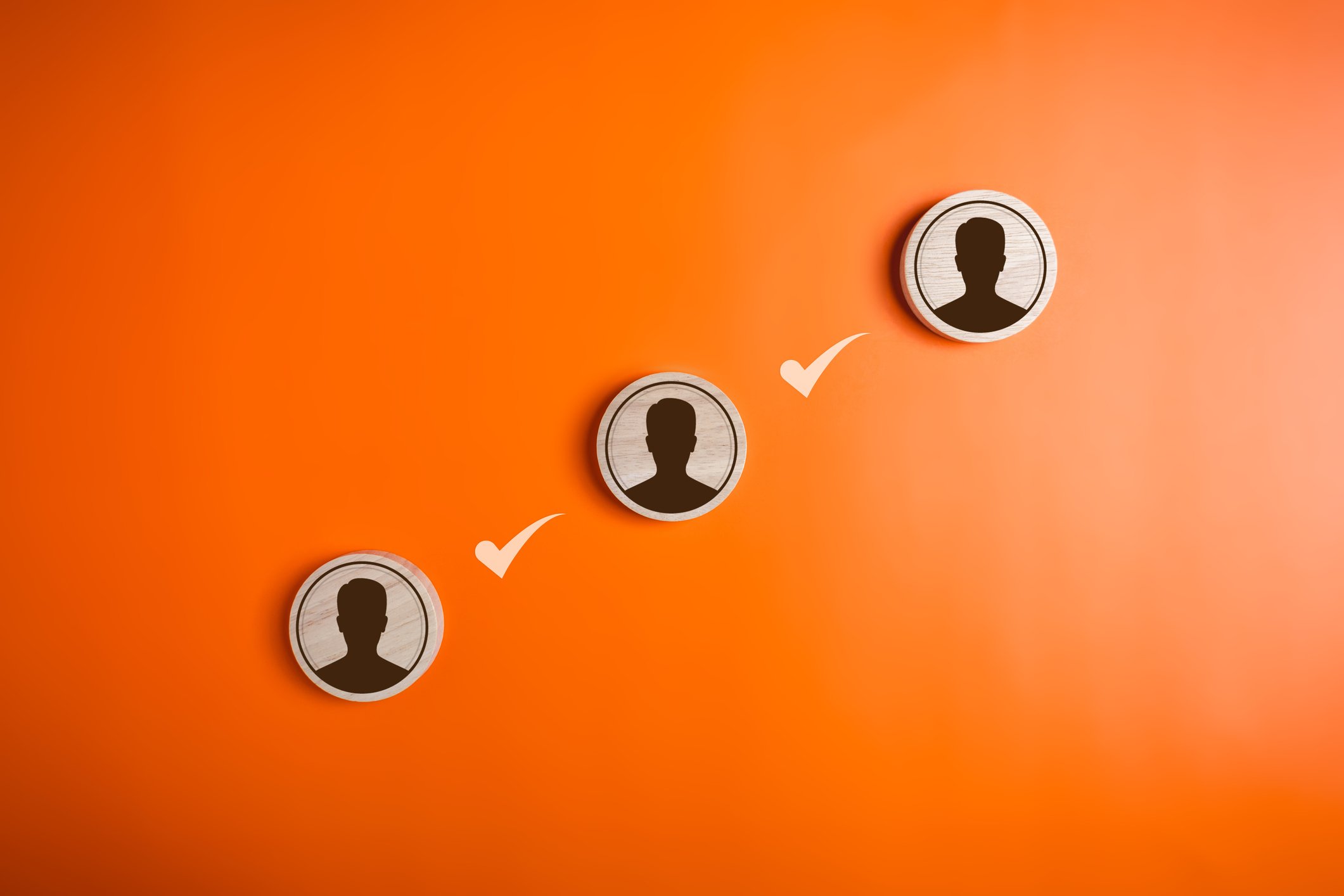 Graphic of three faceless profiles aimed diagonally to the right with two check marks in between them Orange background
