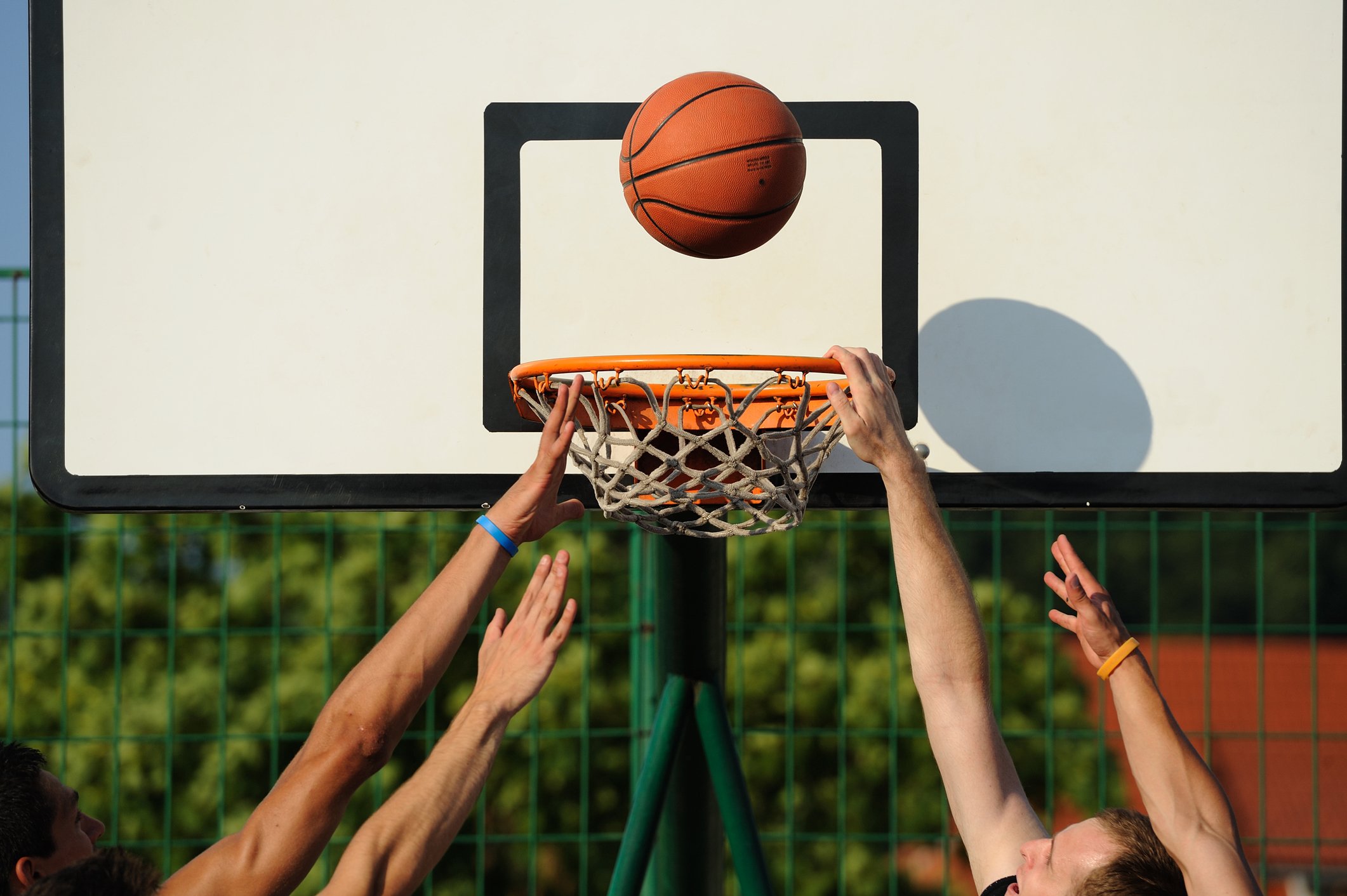 Photo of four hands going up for a rebound as a basketball floats above the rim