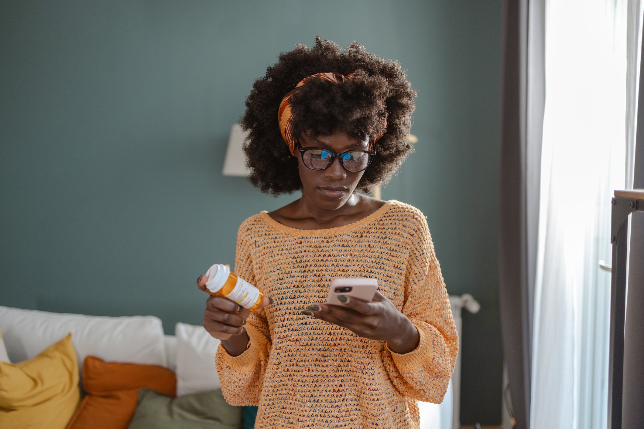 woman at home holding medication using smartphone