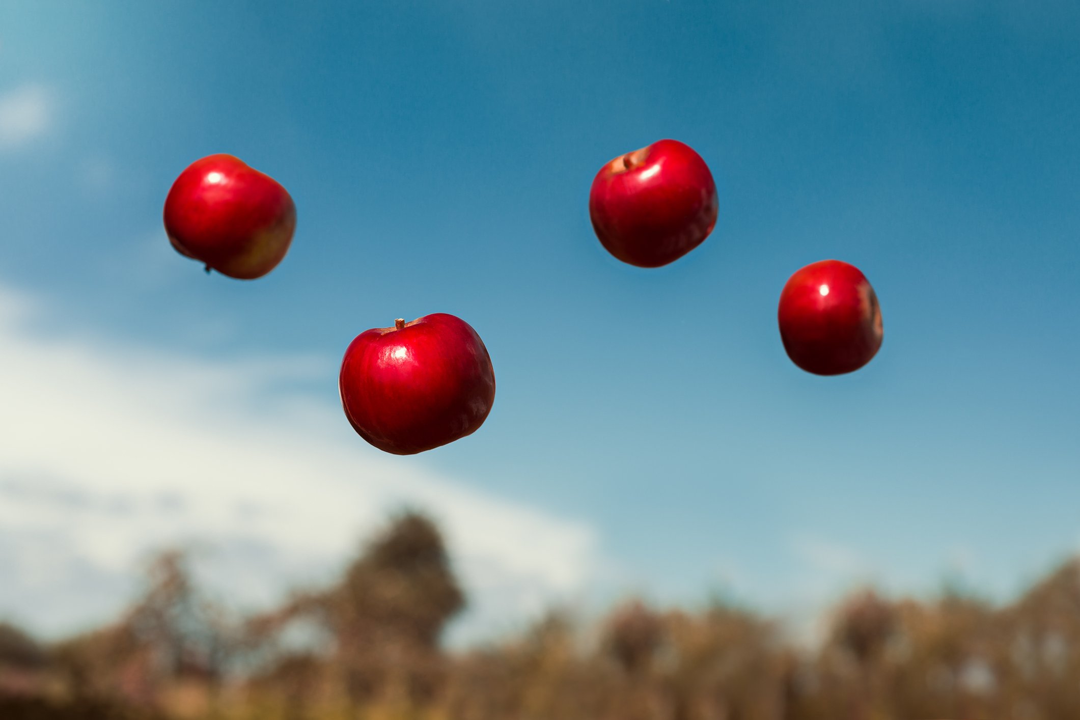A photo of four apples suspended in the air blue sky out of focus in the background