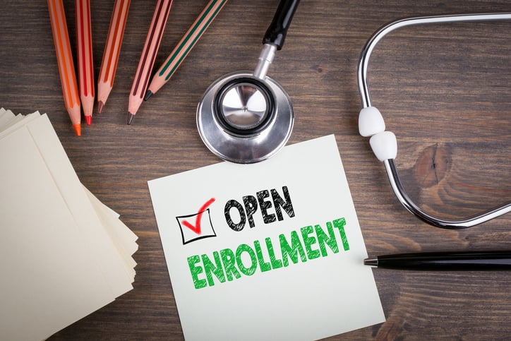 A piece of paper that reads open enrollment with a stethoscope and pencils
