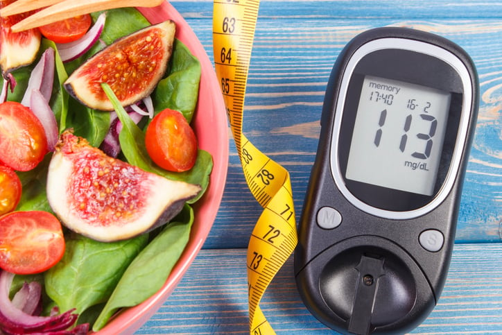 A glucose monitor next to a measuring tape and a fig salad