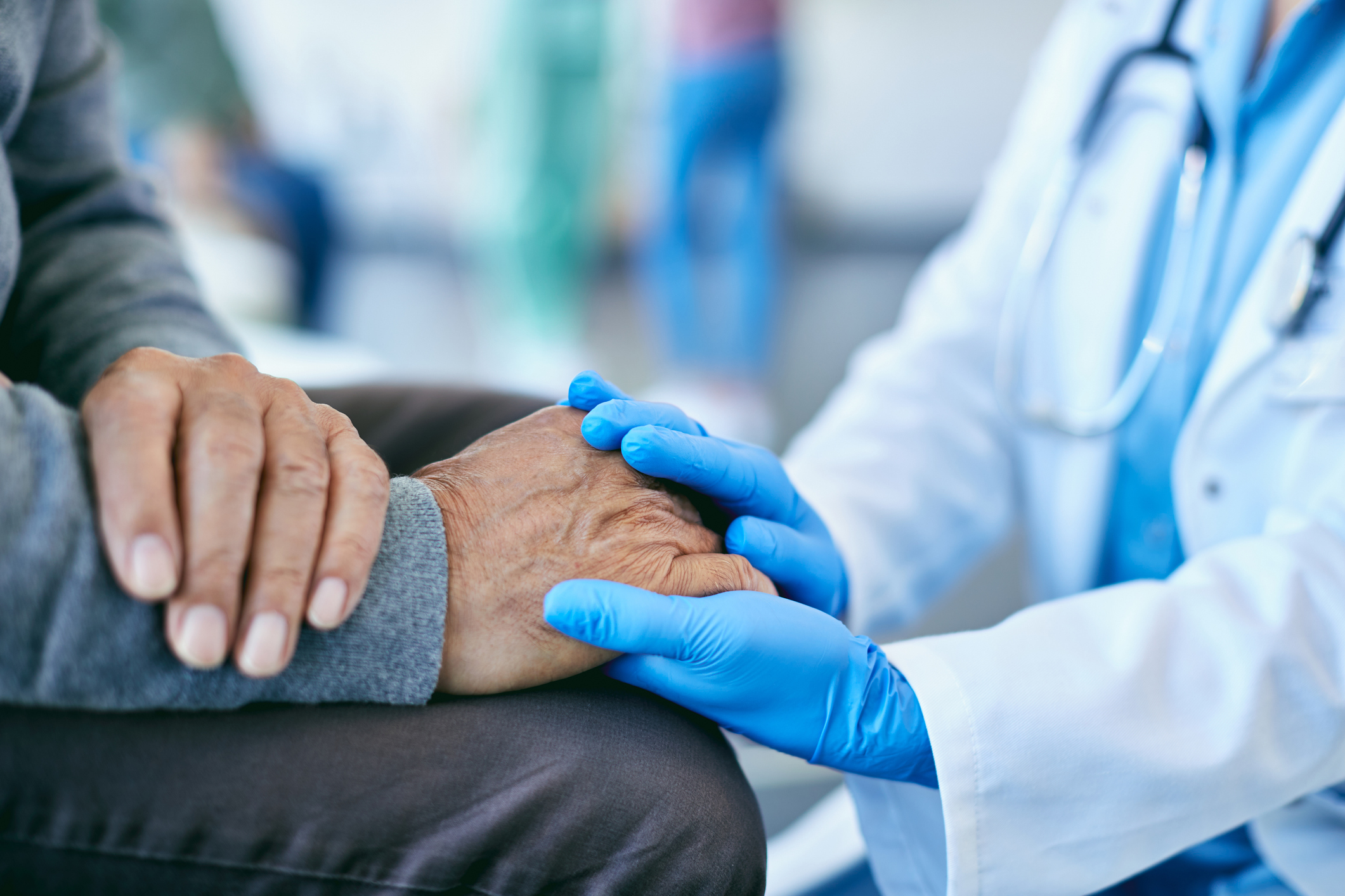 Close-up of healthcare worker consoling mature patient and holding his hand at medical clinic