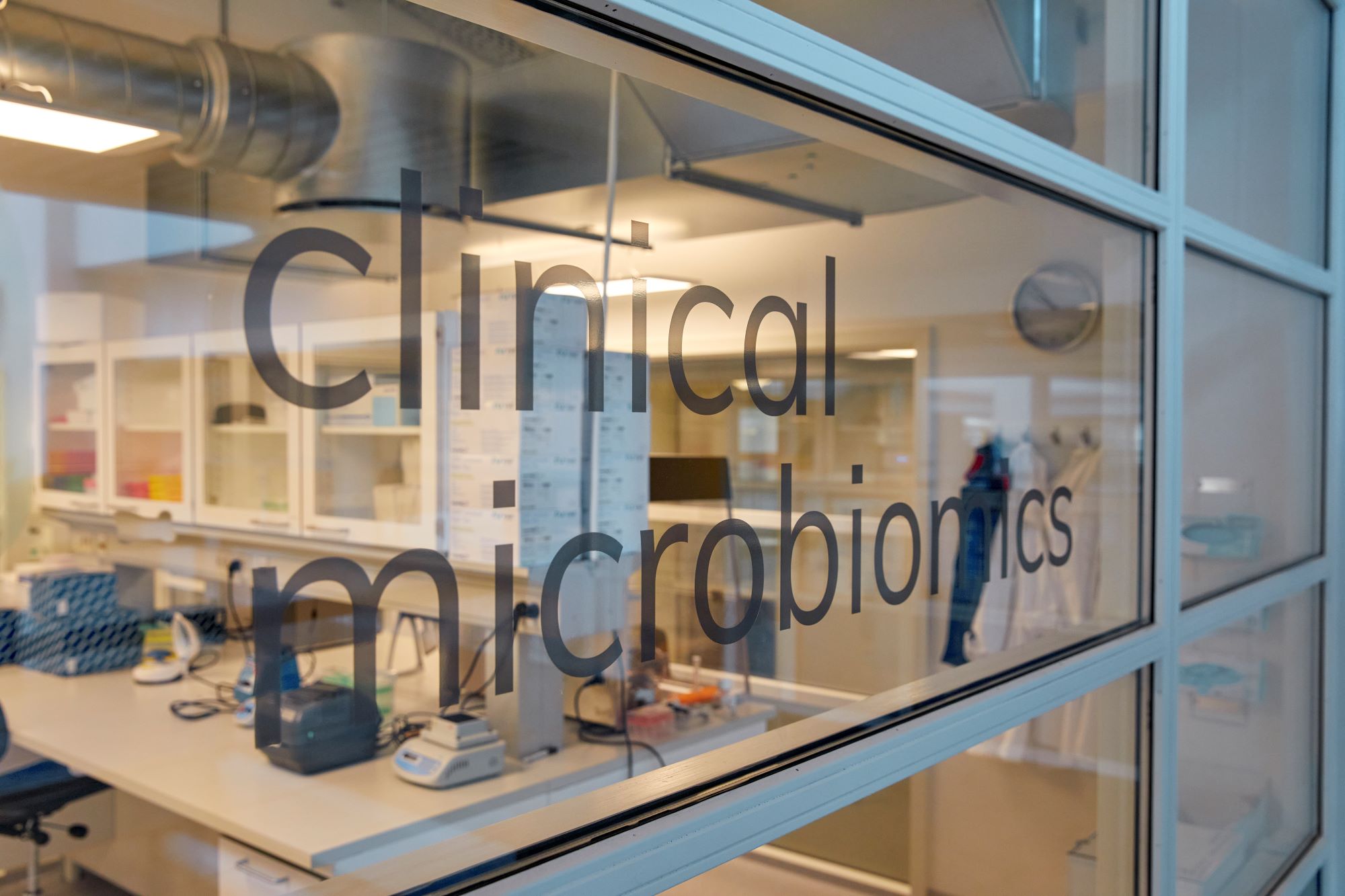 A window into laboratory of Clinical Microbiomics The company logo is on the glass beyond it you can see computers 