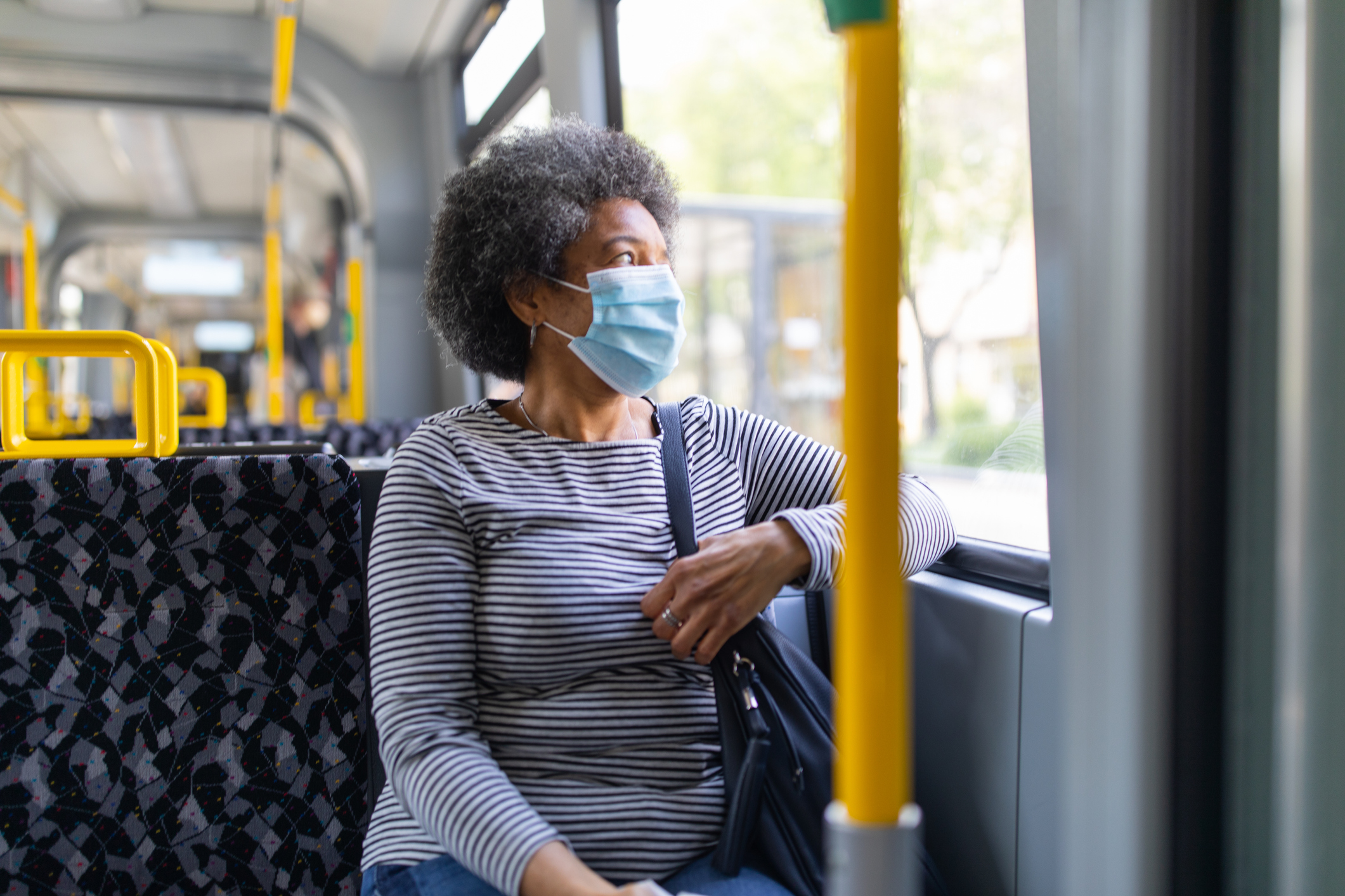A woman rides a bus while wearing a face mask