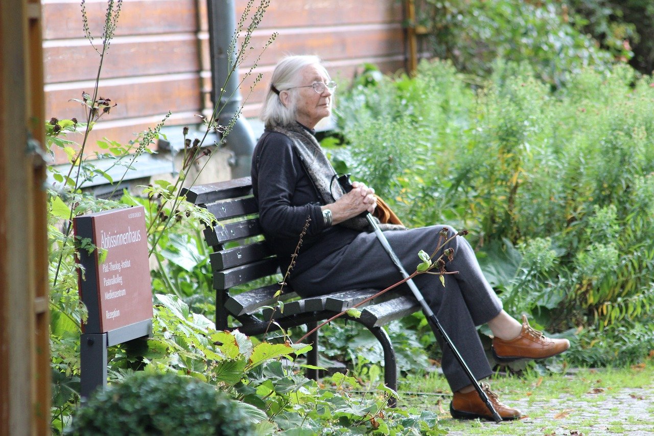 old woman sitting on a bench in a garden holding a cane