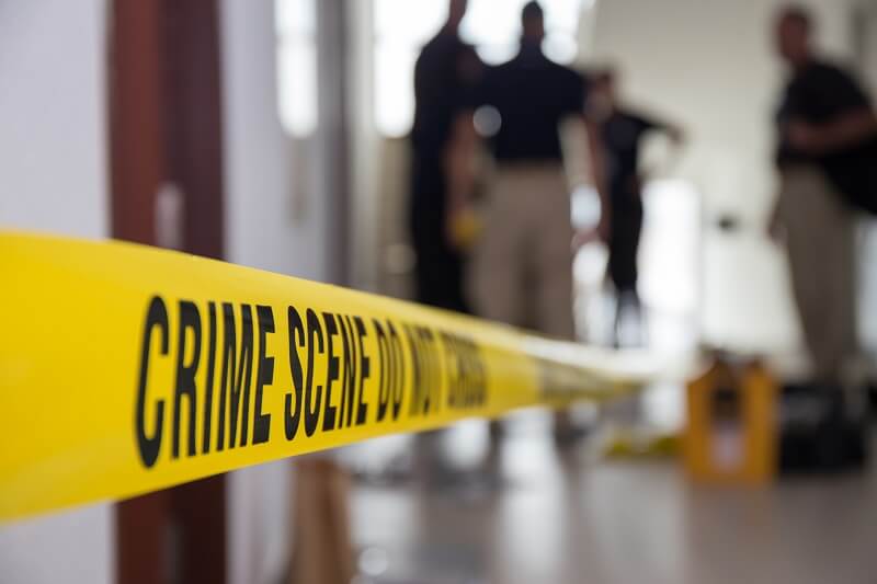 Crime scene tape in a building with blurred forensic team in background