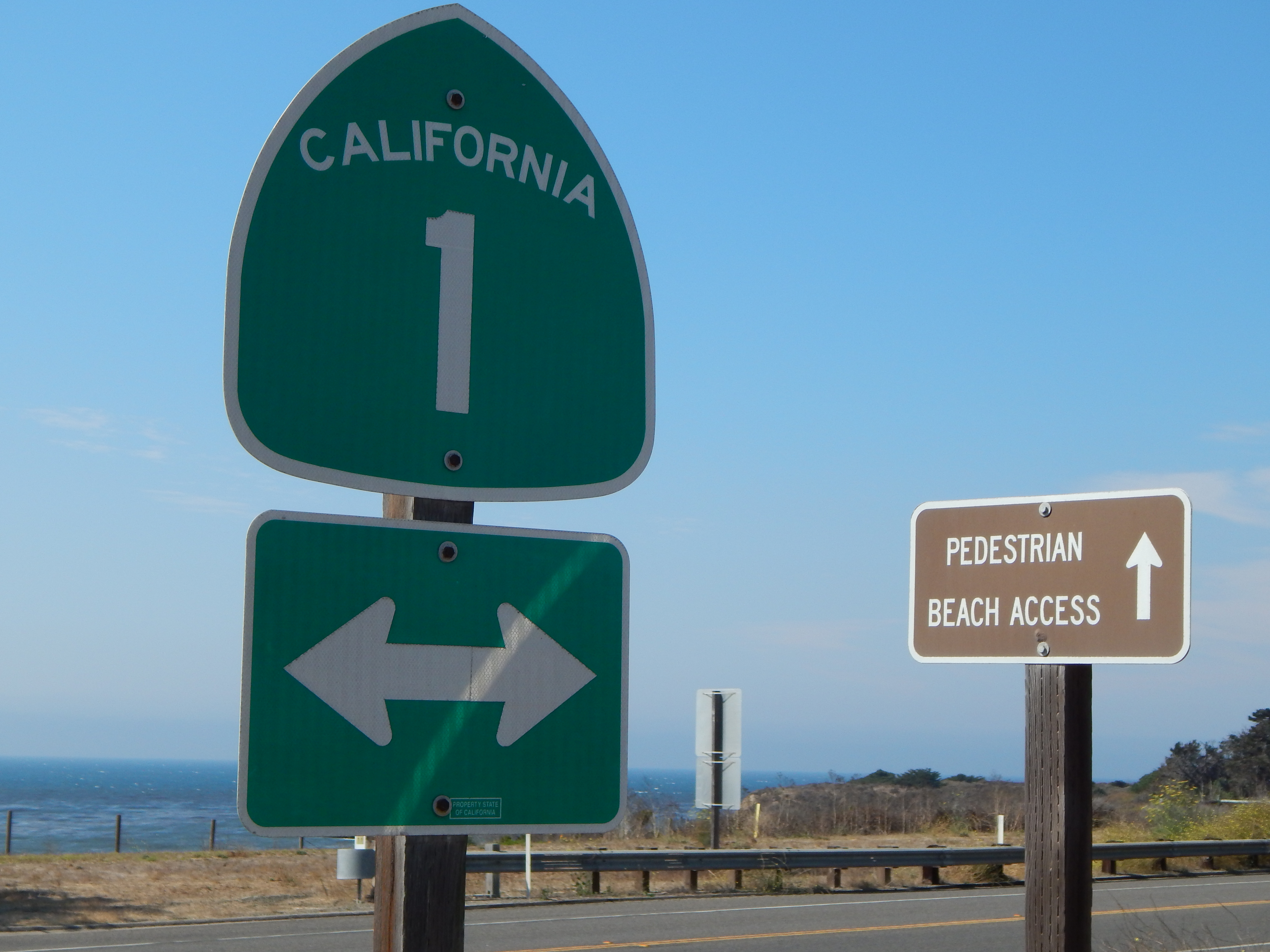 Sign for the 1 freeway and sign reading pedestrian beach access both with arrows in California with beach in backgroun