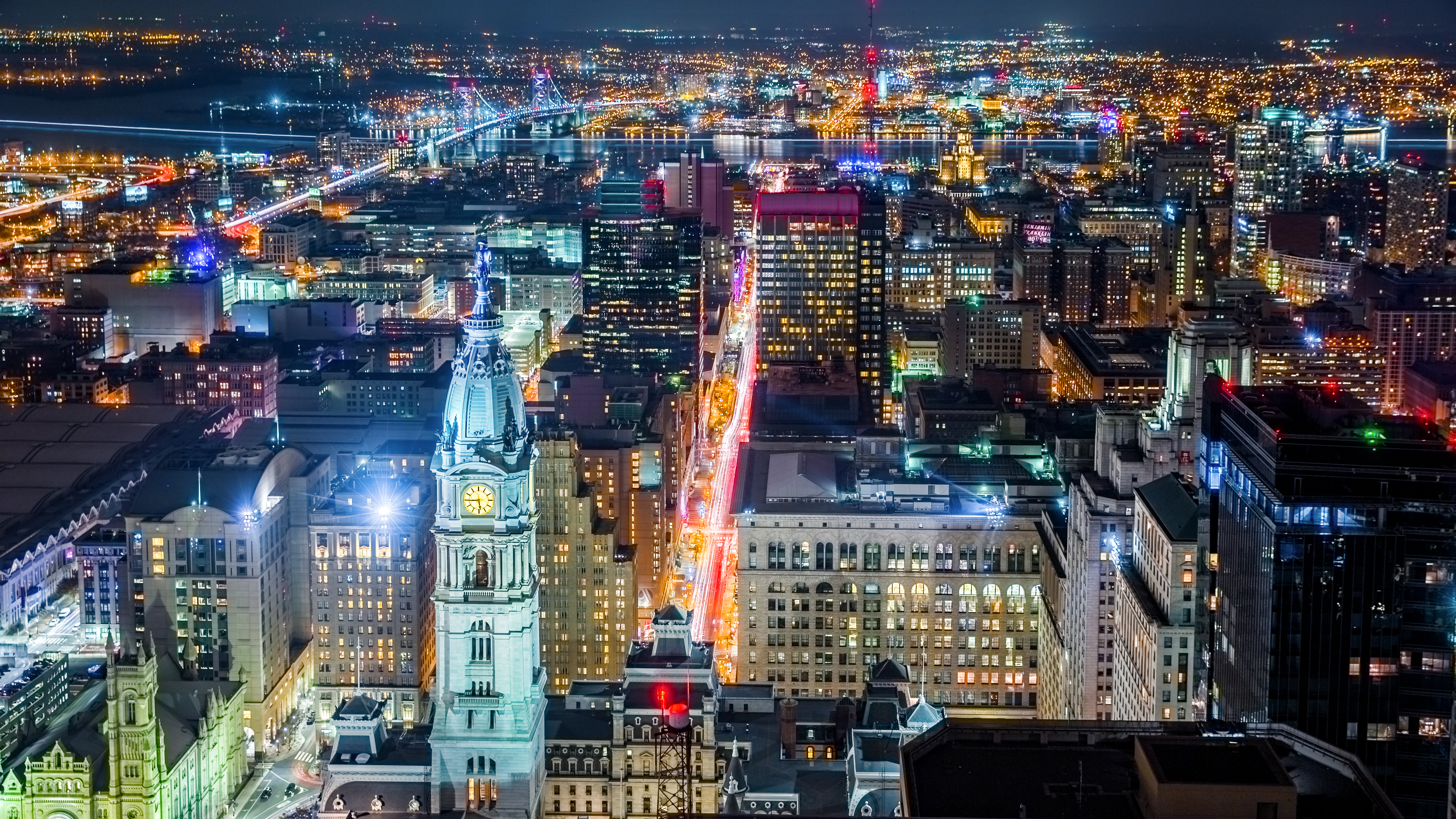 Aerial Philadelphia cityscape by night with the City Hall tower in the foreground and Ben Franklin bridge spanning Delaware r