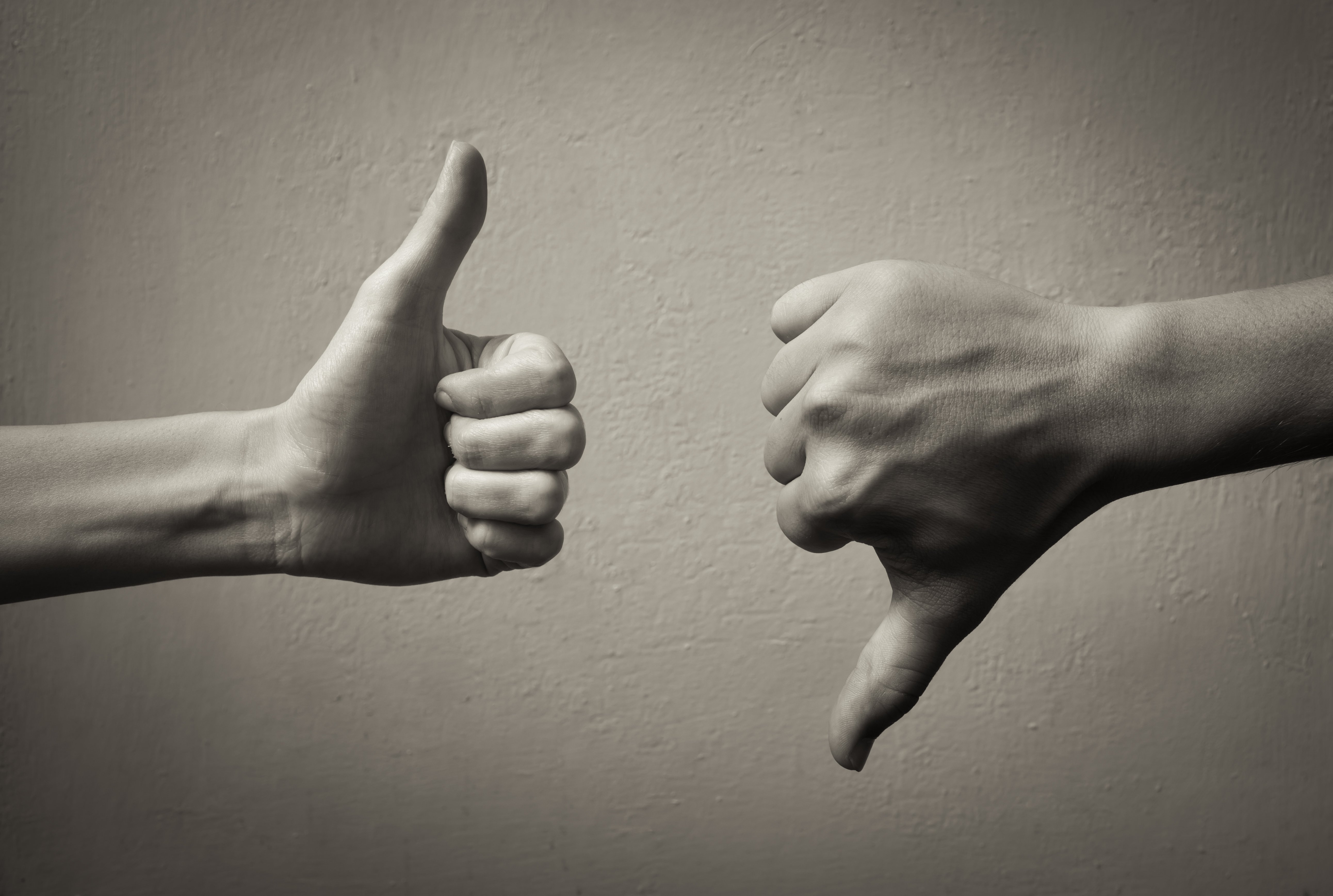 Black-and-white image of a thumbs-up hand and a thumbs-down hand in front of a blank wall