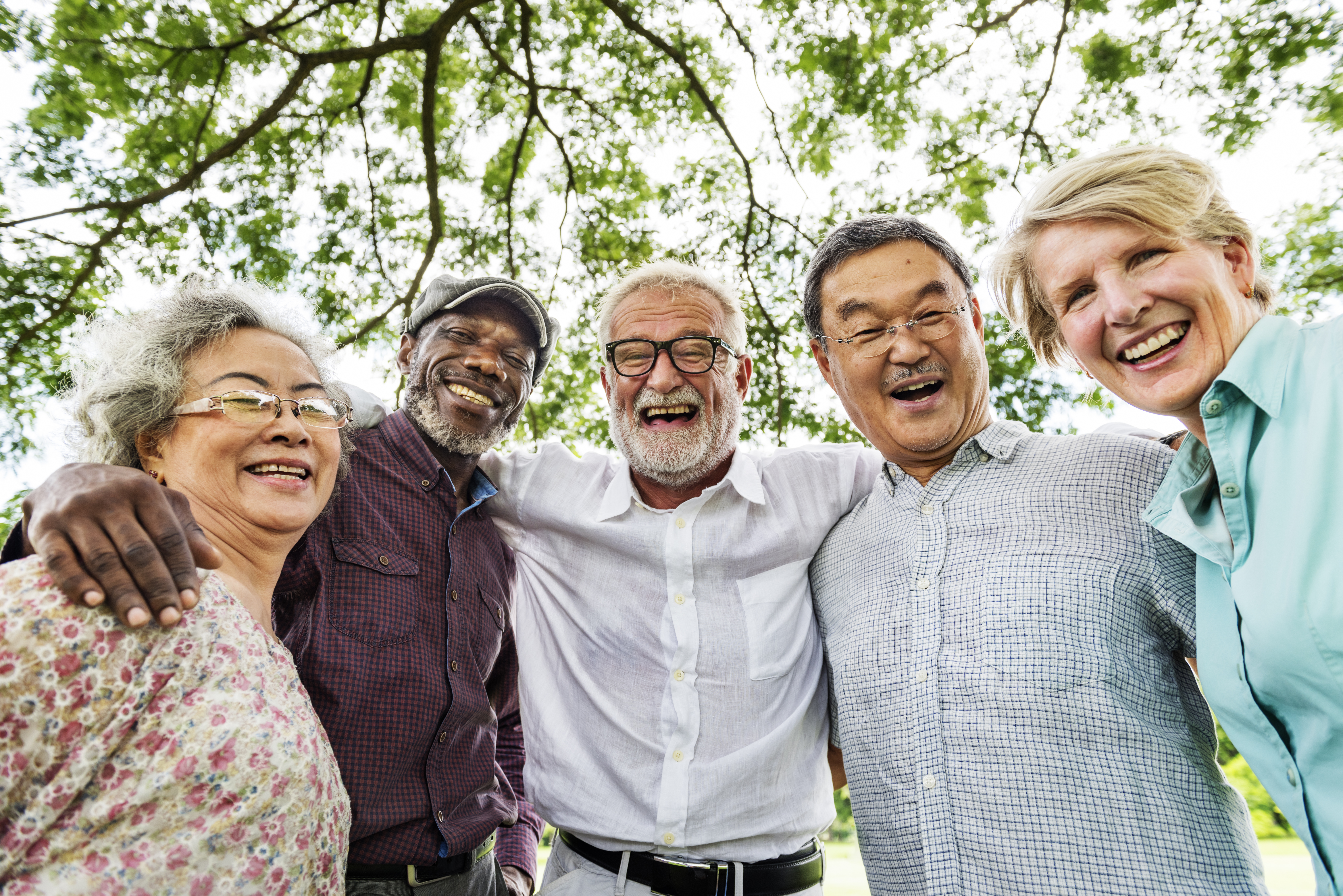 Diverse group of male and female seniors with arms around each other smiling at camera