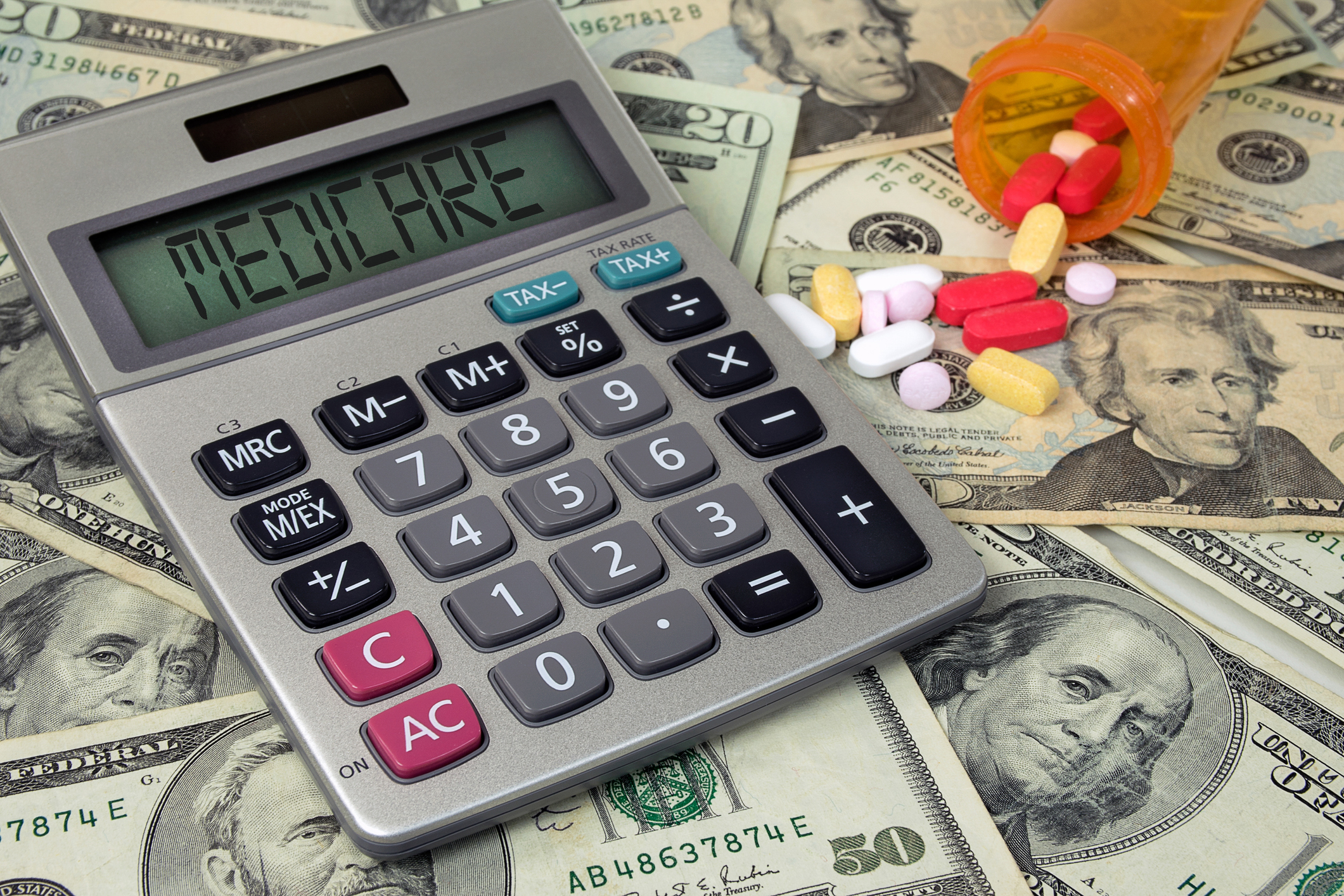 Calculator that says Medicare on it on top of money next to bottle of pills
