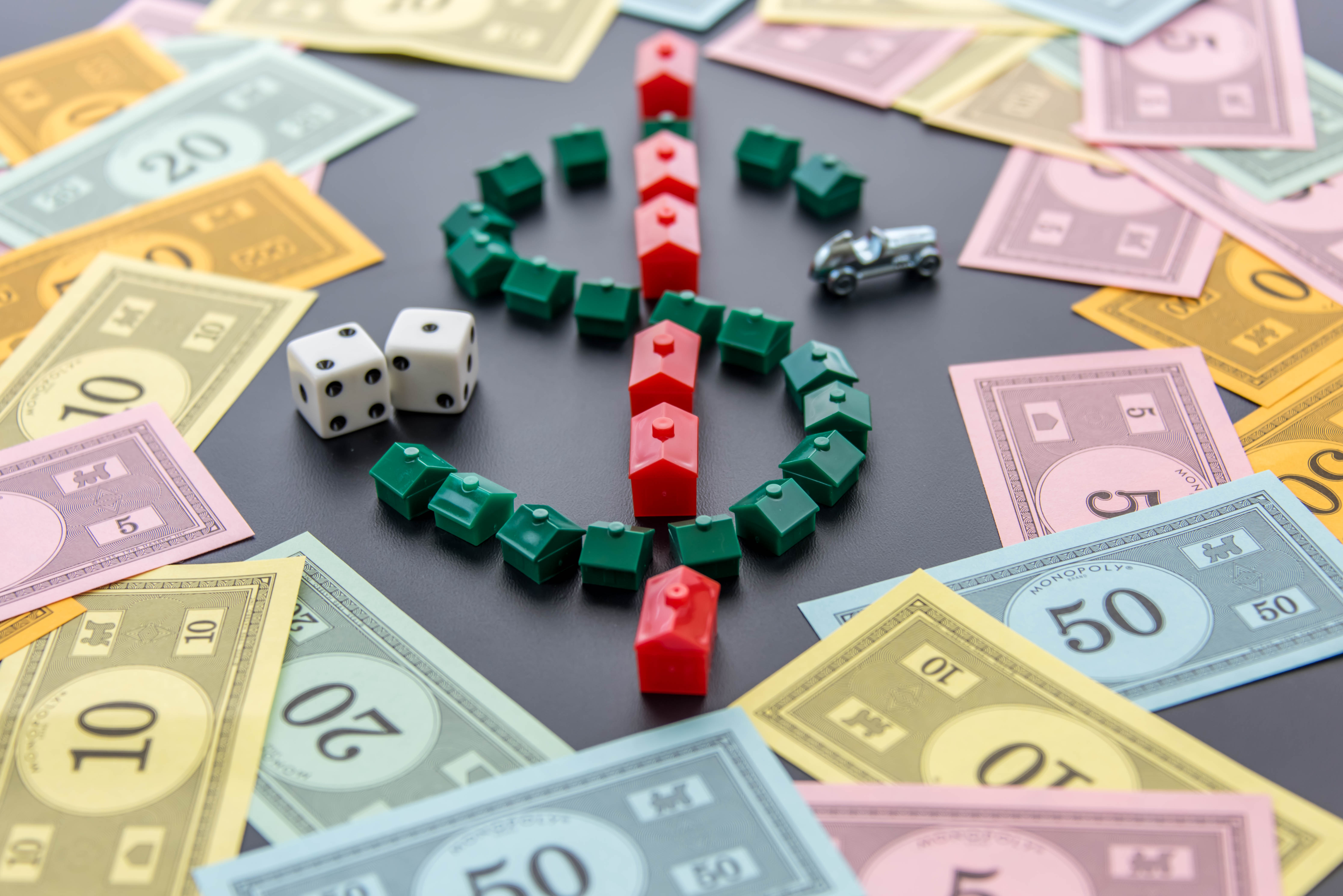 A dollar sign created by Monopoly game houses is surrounded by Monopoly money Dice and the car token appear next to the doll
