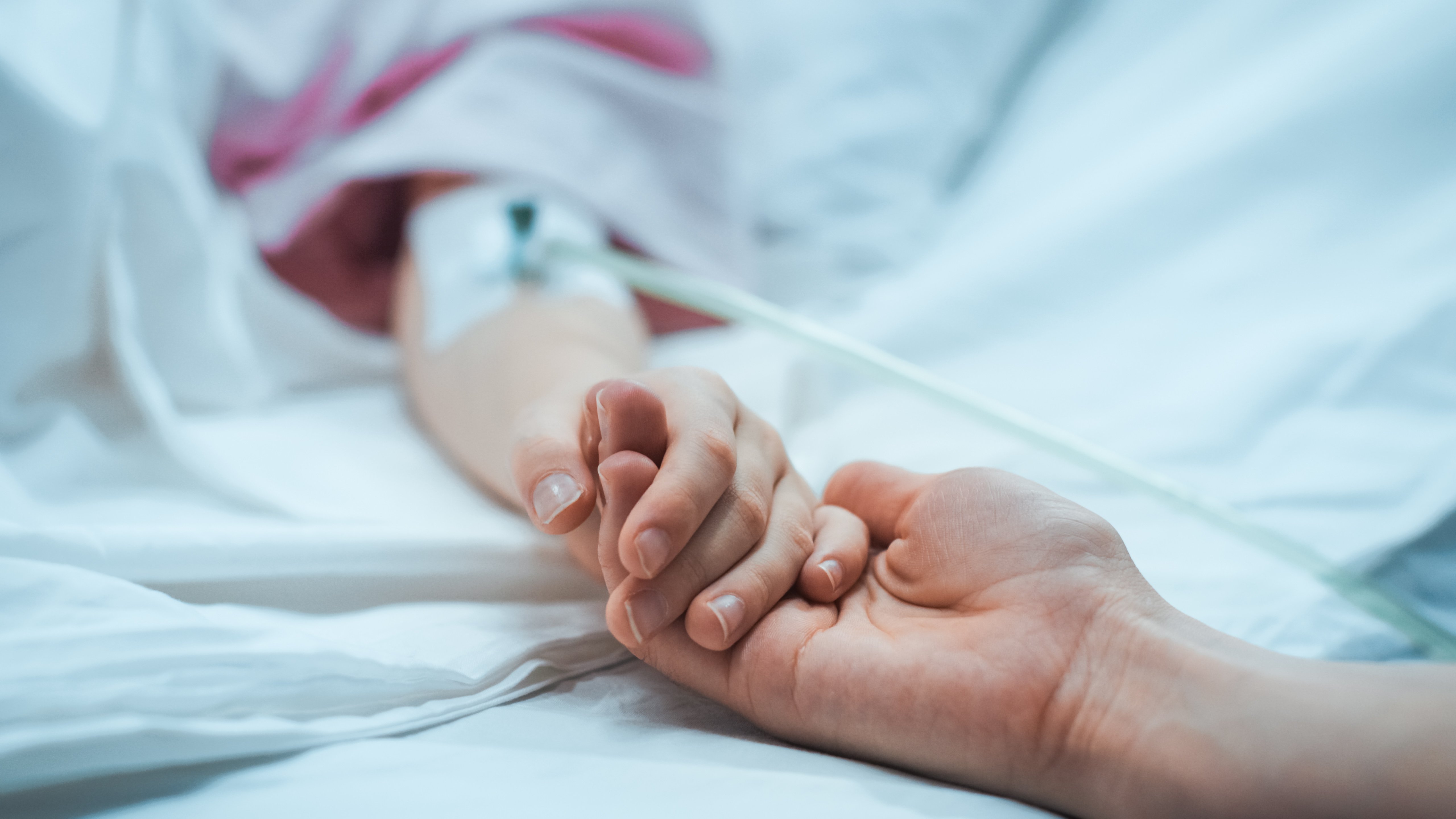 photo of child lying in the hospital bed sleeping with parent holding the childs hand comforting