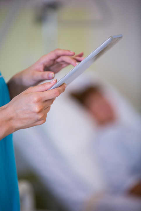 close up of a nurses hands using a tablet inside a hospital room