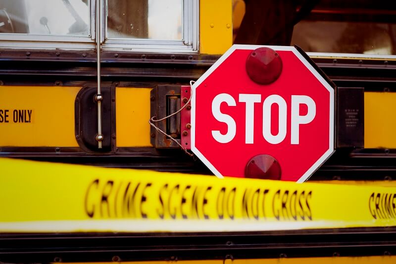 The side of a school bus with cordon tape that reads CRIME SCENE DO NOT CROSS