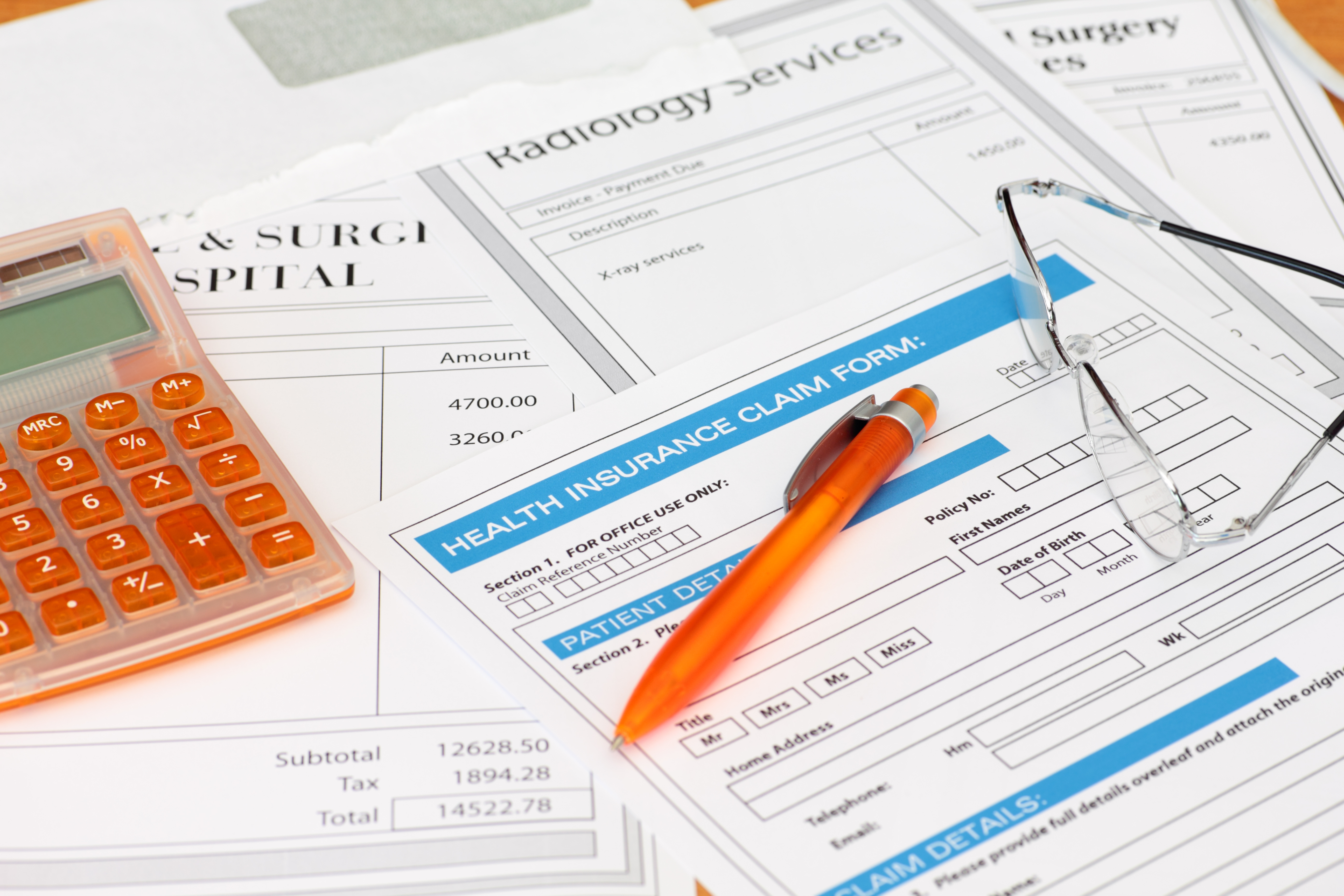 A stack of medical bills and claims forms with a calculator