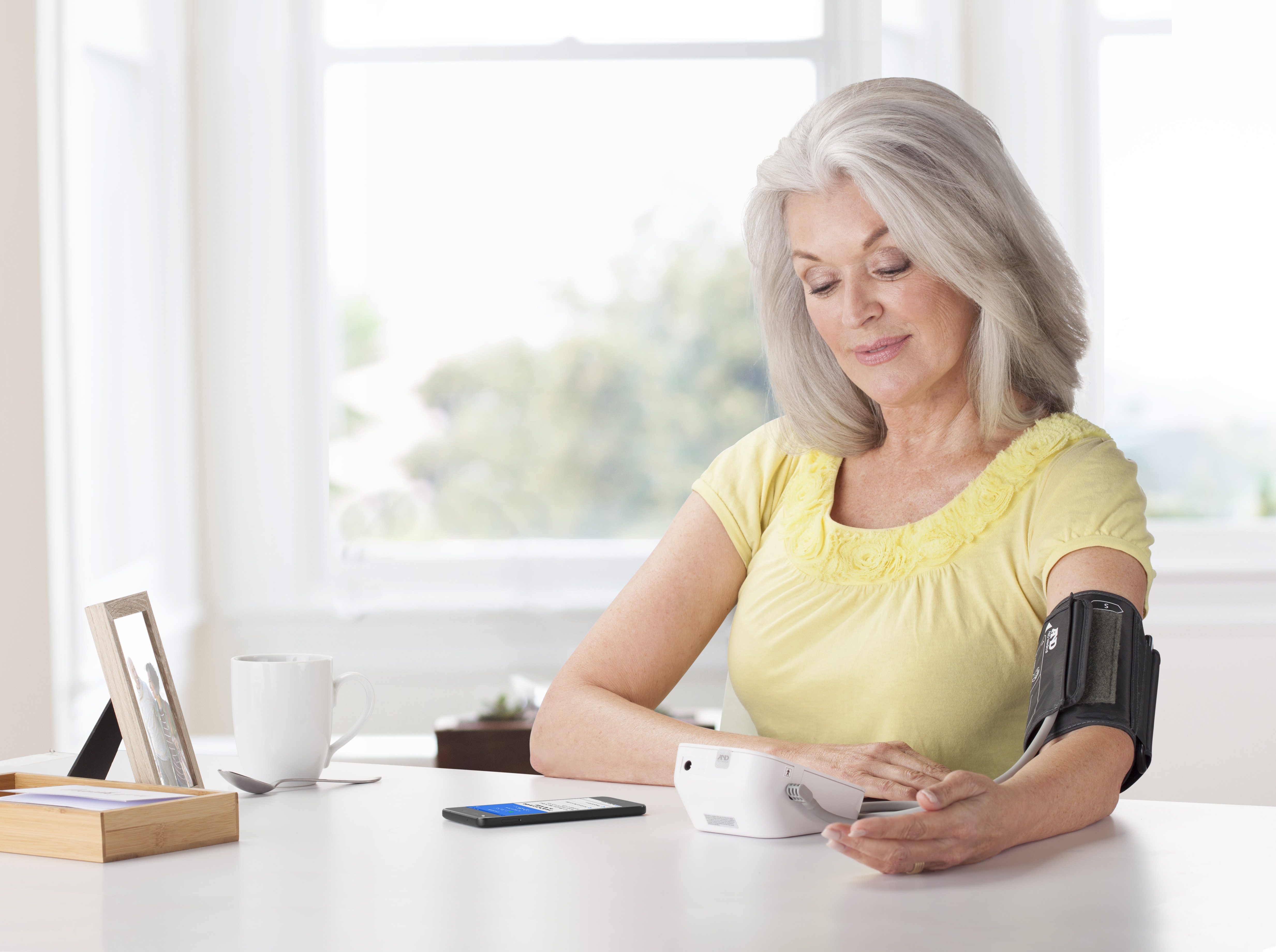 Senior woman sitting at a table using blood pressure monitor device