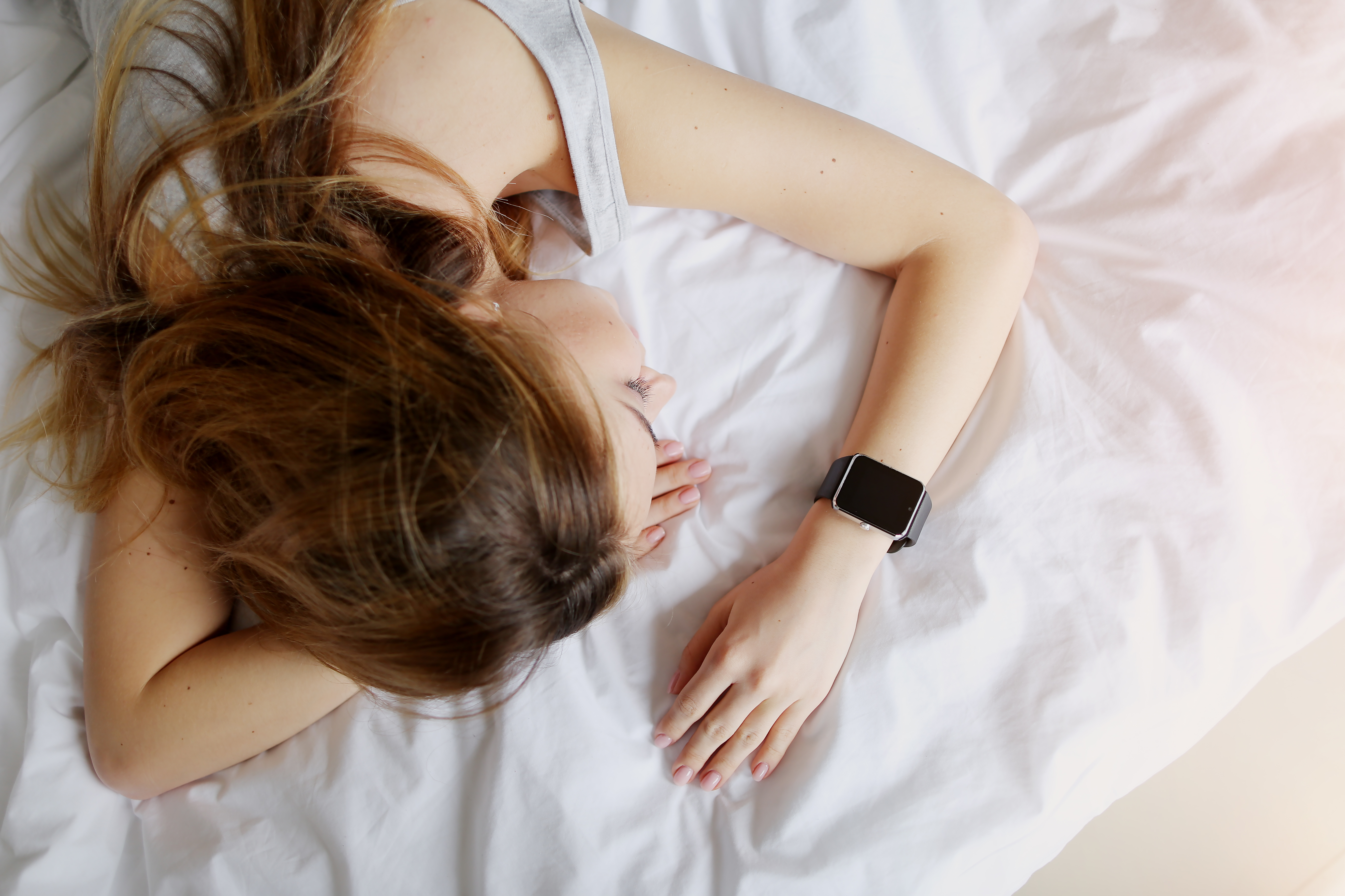 A woman sleeping on a white bed and wearing a smartwatch